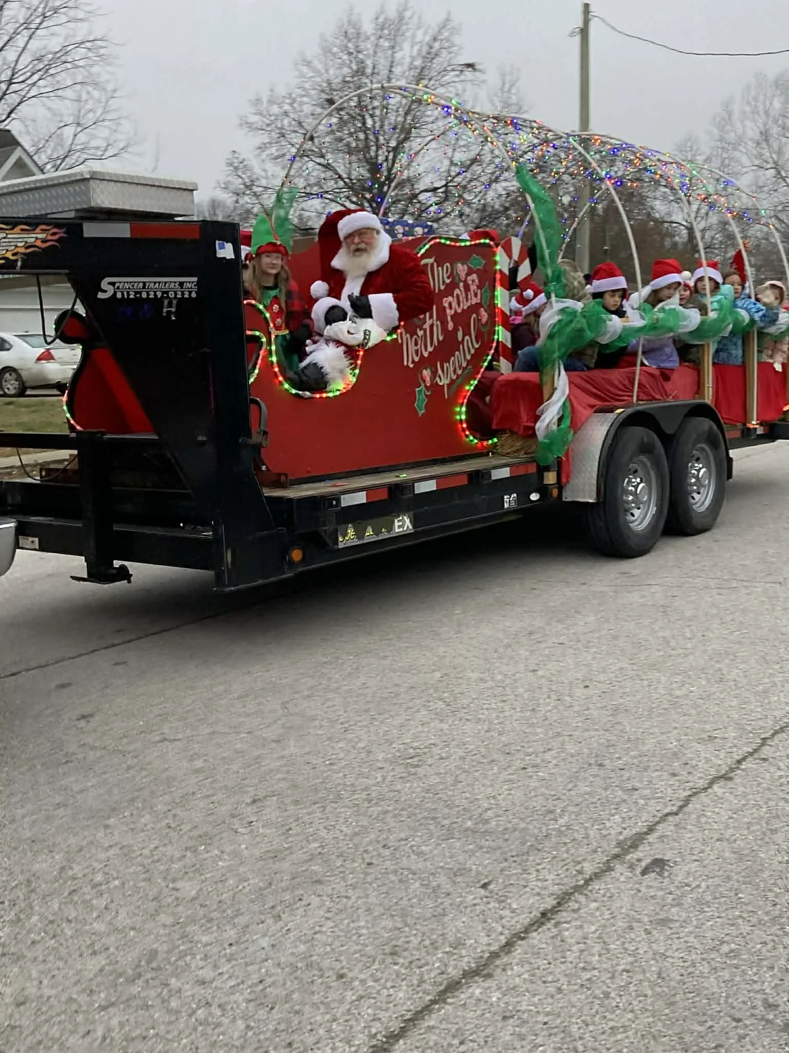A Christmas parade float with Santa Claus and children dressed as elves, decorated with colorful lights and festive banners.