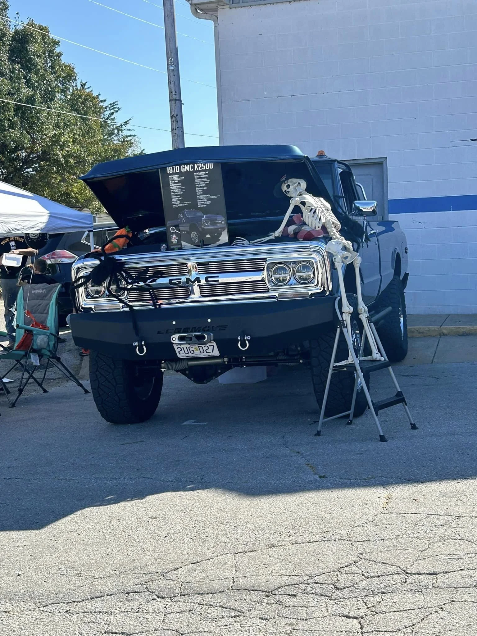 Display of a classic black GMC truck with its hood open, decorated with Halloween skeleton and ghost figures, at an outdoor event.