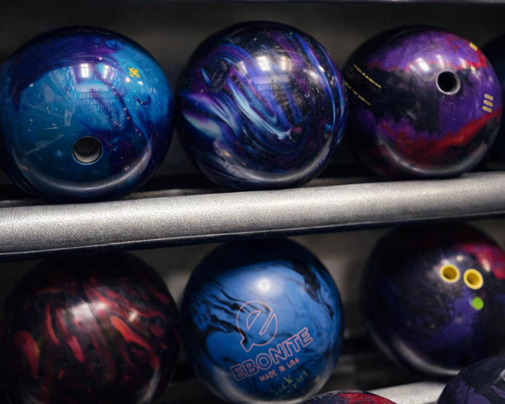 Six bowling balls with colorful, swirling designs on a metal rack in a bowling alley.