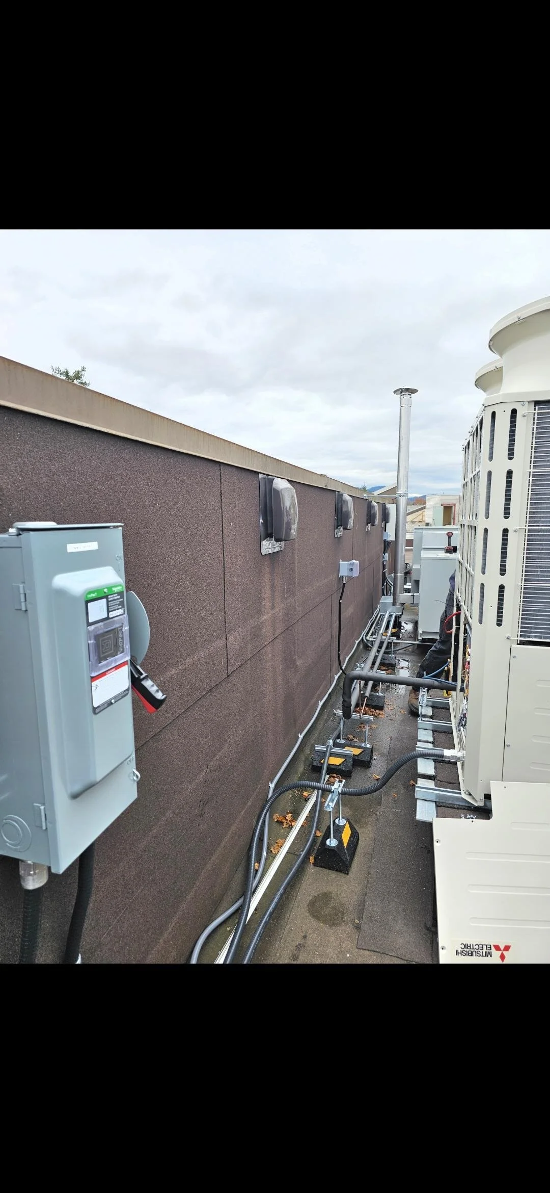 Rooftop HVAC units and electrical boxes on a building rooftop with pipes and wiring.