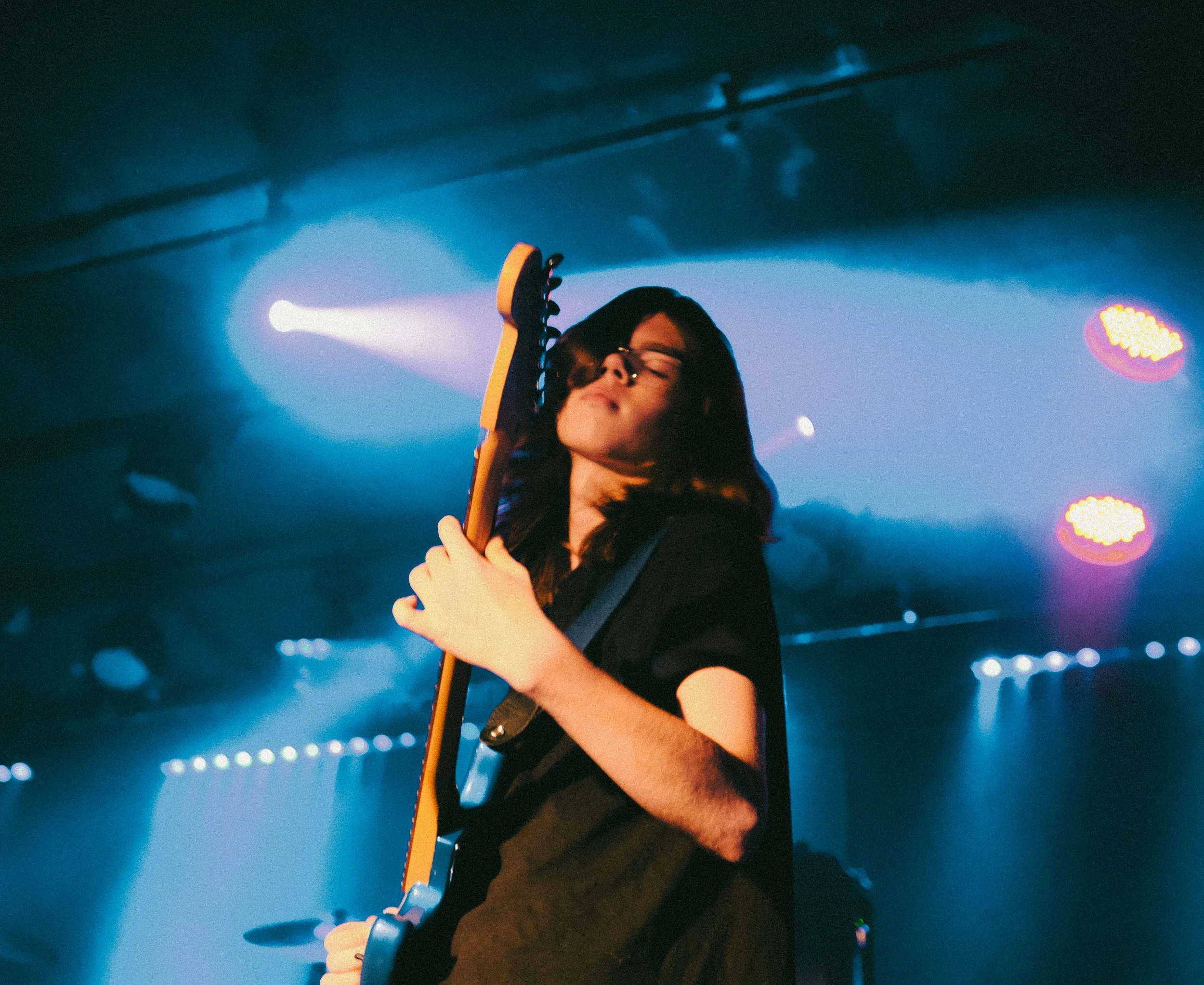 Person holding a guitar on stage with colorful lights in the background.