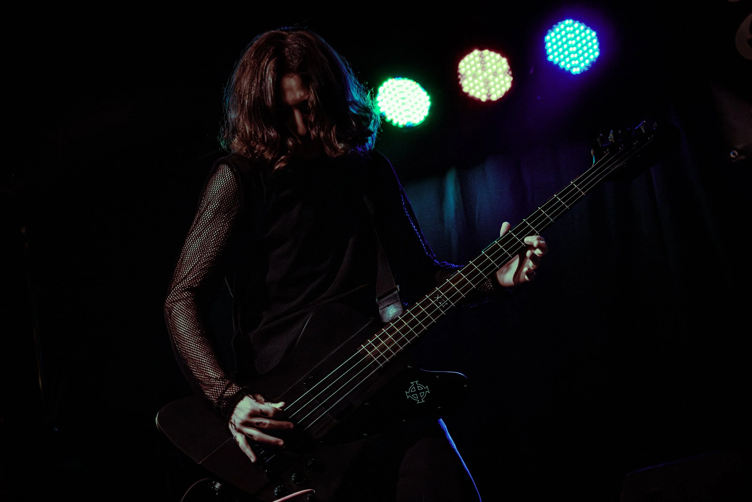 Person playing an electric bass guitar on stage with colorful LED lights in the background.