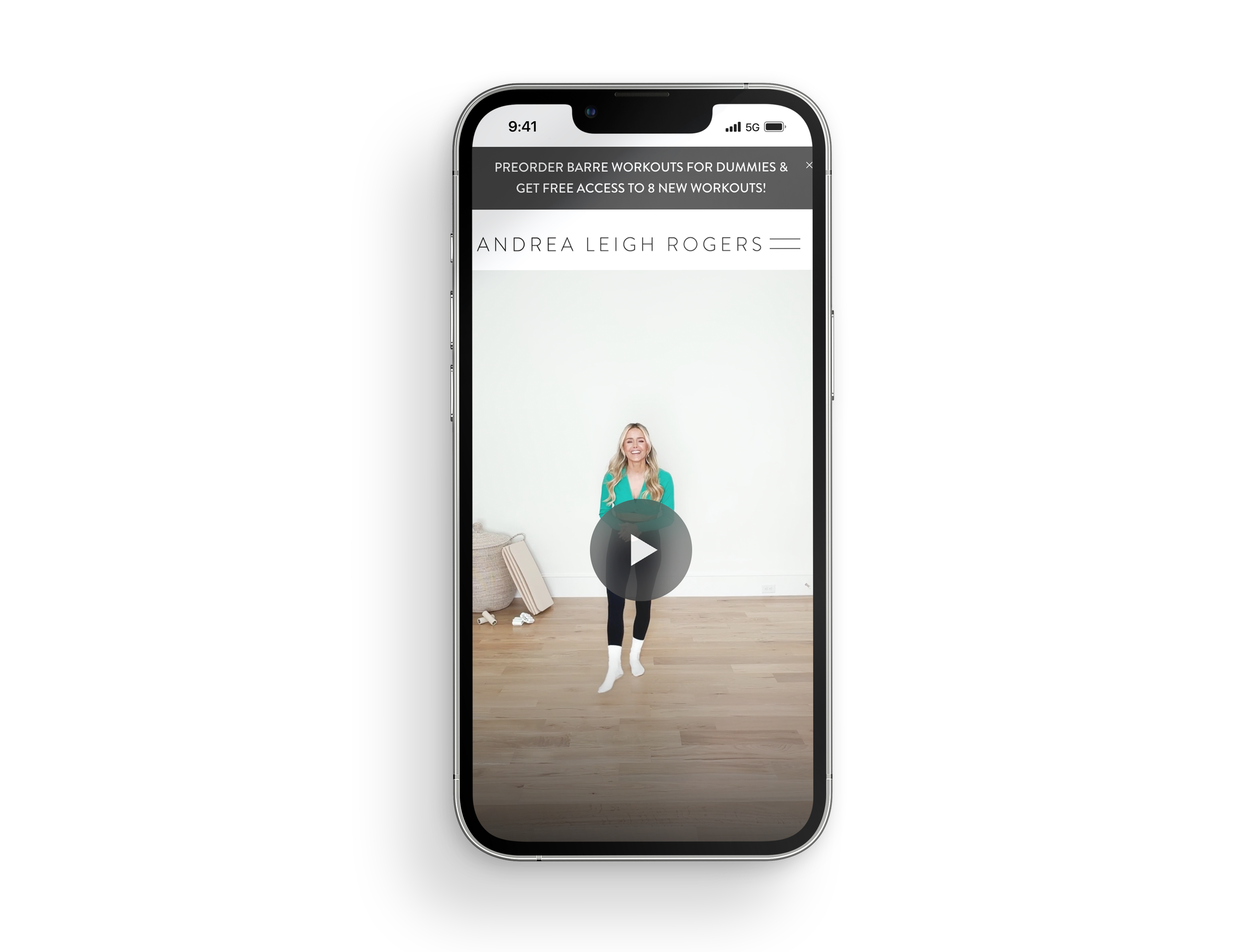 Smartphone screen displaying a woman smiling and jumping in a home workout video titled 'Andrea Leigh Rogers' with a play button overlay.