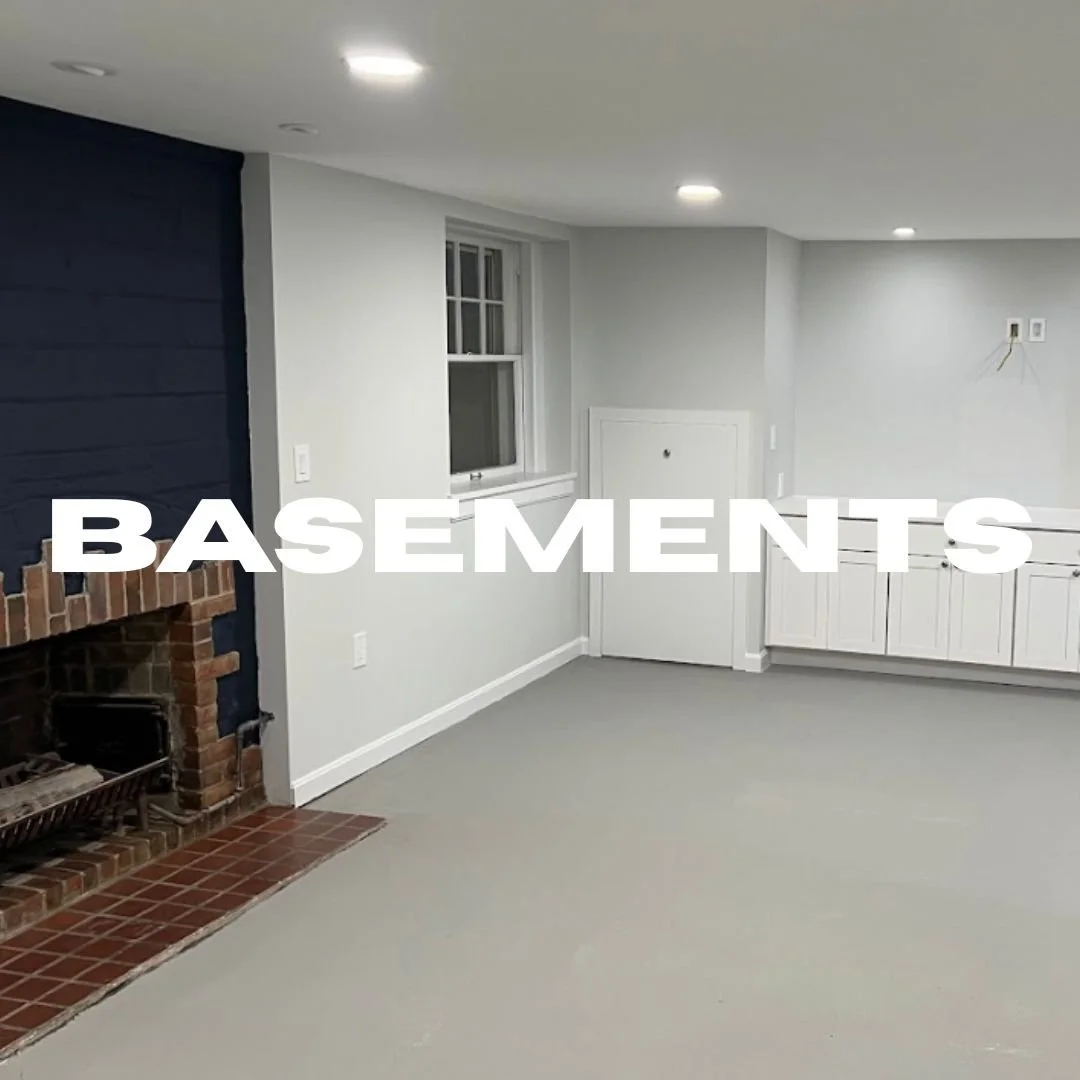 Interior of a finished basement with gray walls, white cabinets, a brick fireplace, and a small window. The word 'BASEMENTS' is overlaid in large white text.