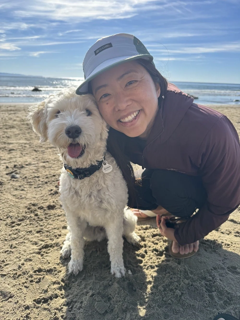 Therapist Ingrid Nishimoto smiling with her dog on the beach.