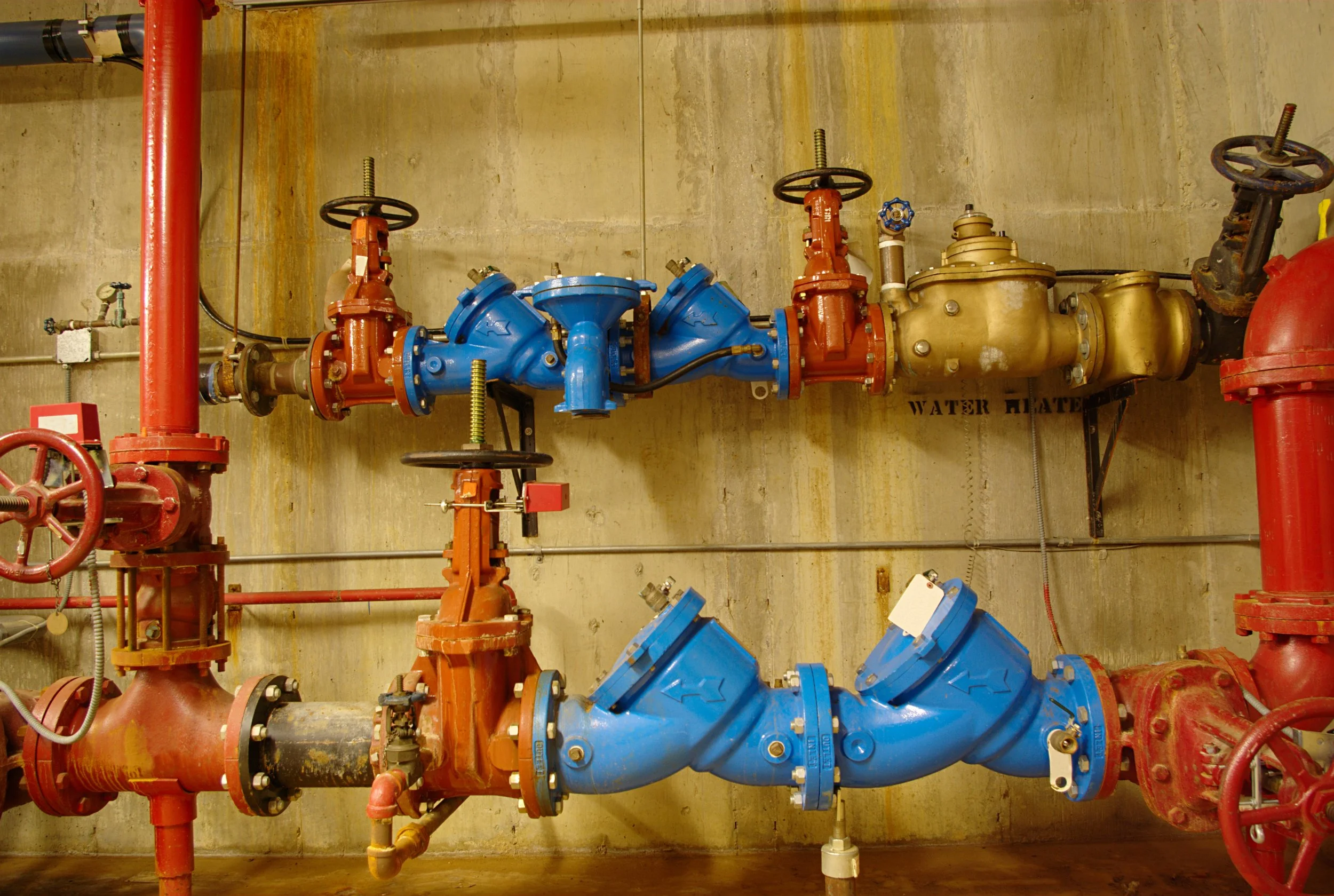 Industrial water pipes and valves in a utility room.