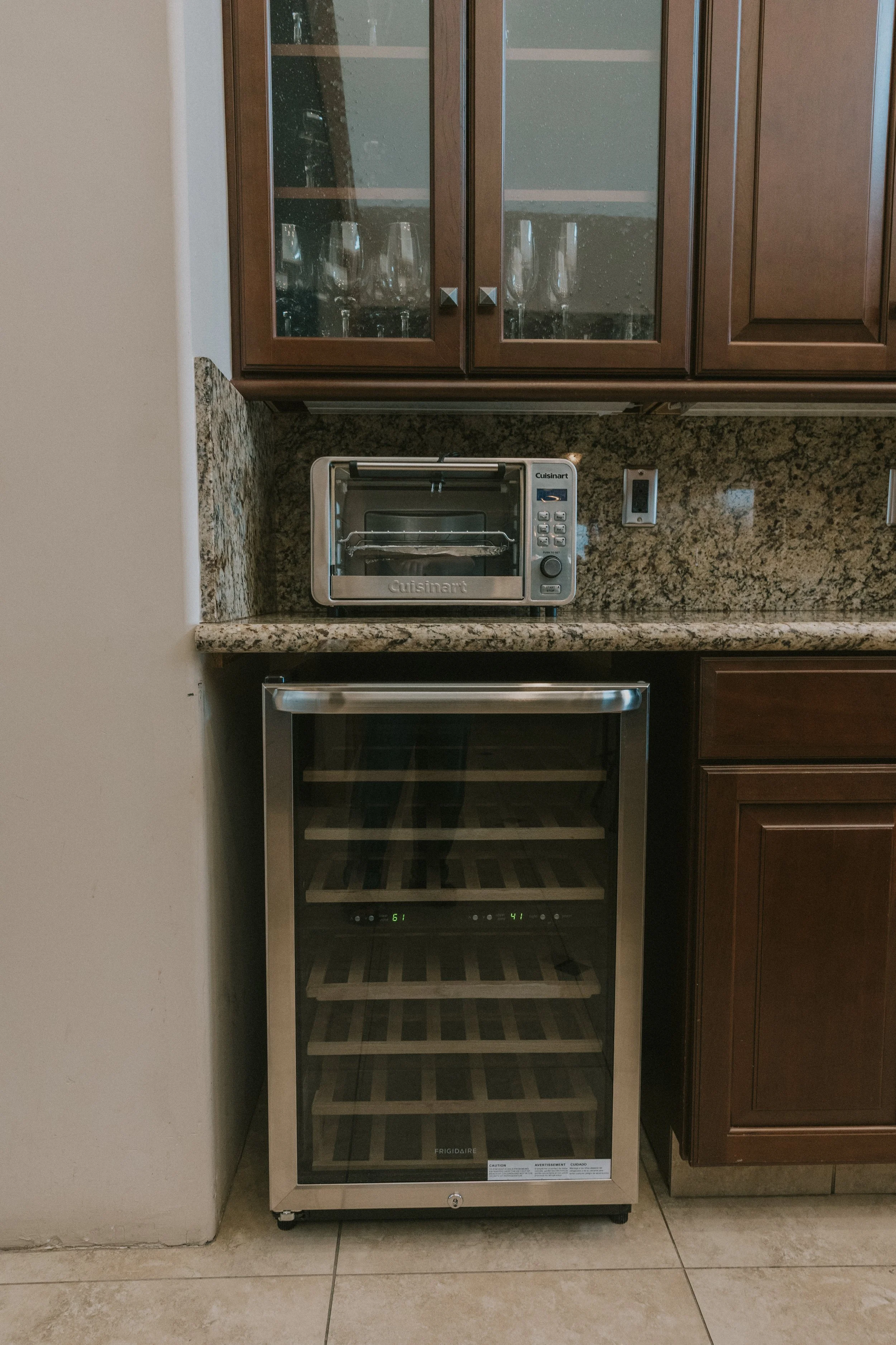 Empty wine cooler with glass door next to kitchen cabinets with glassware inside.