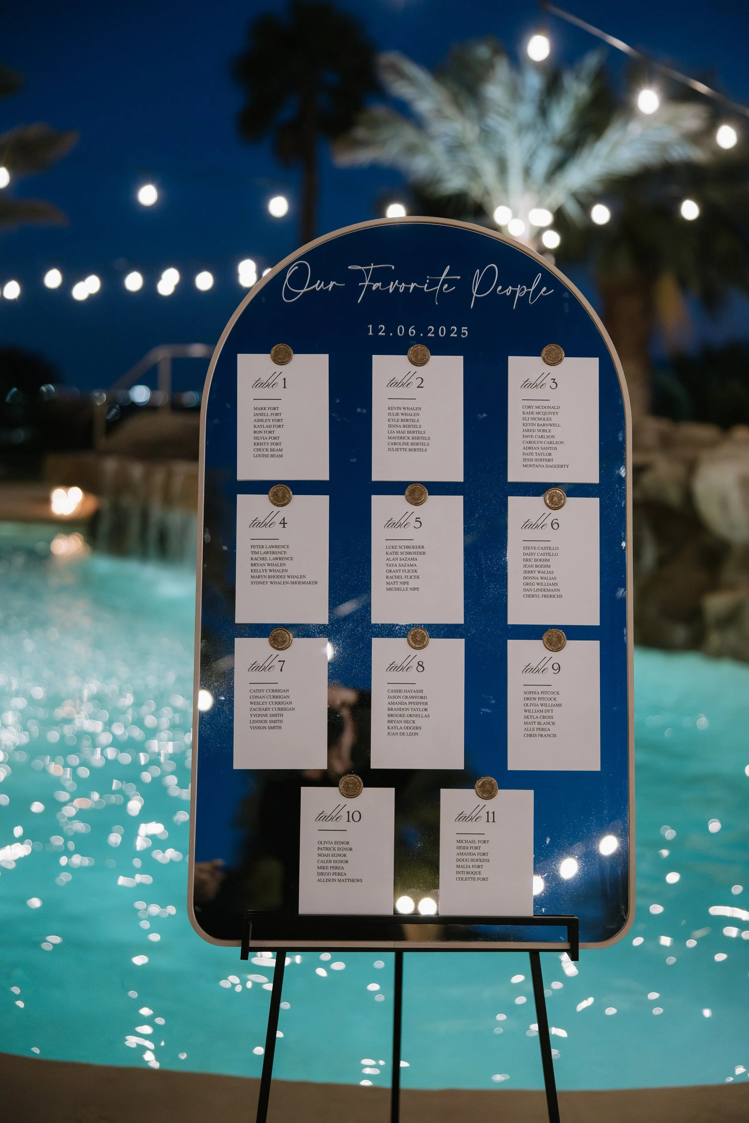 A seating chart for an event, titled "Our Favorite People," displays names of guests at multiple tables, with a nighttime poolside setting and string lights in the background.