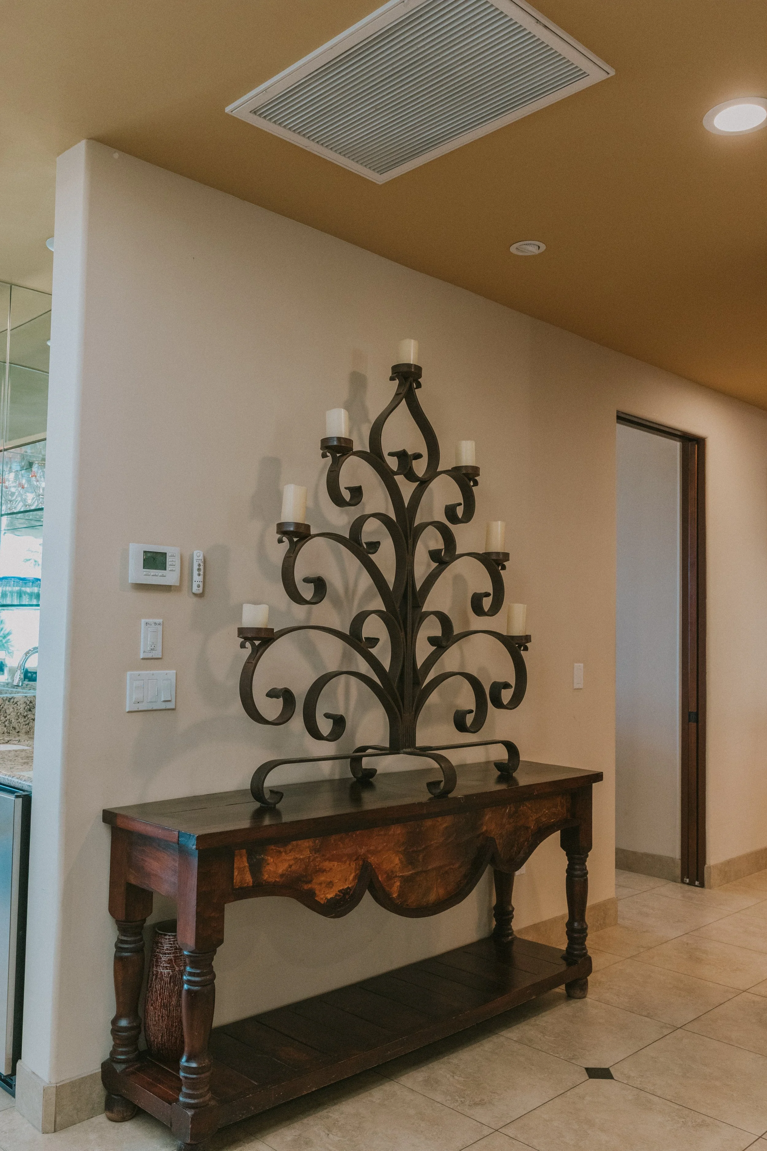 A decorative black metal candle holder with multiple branches and white candles on a wooden table in a room with beige walls and tiled floor.