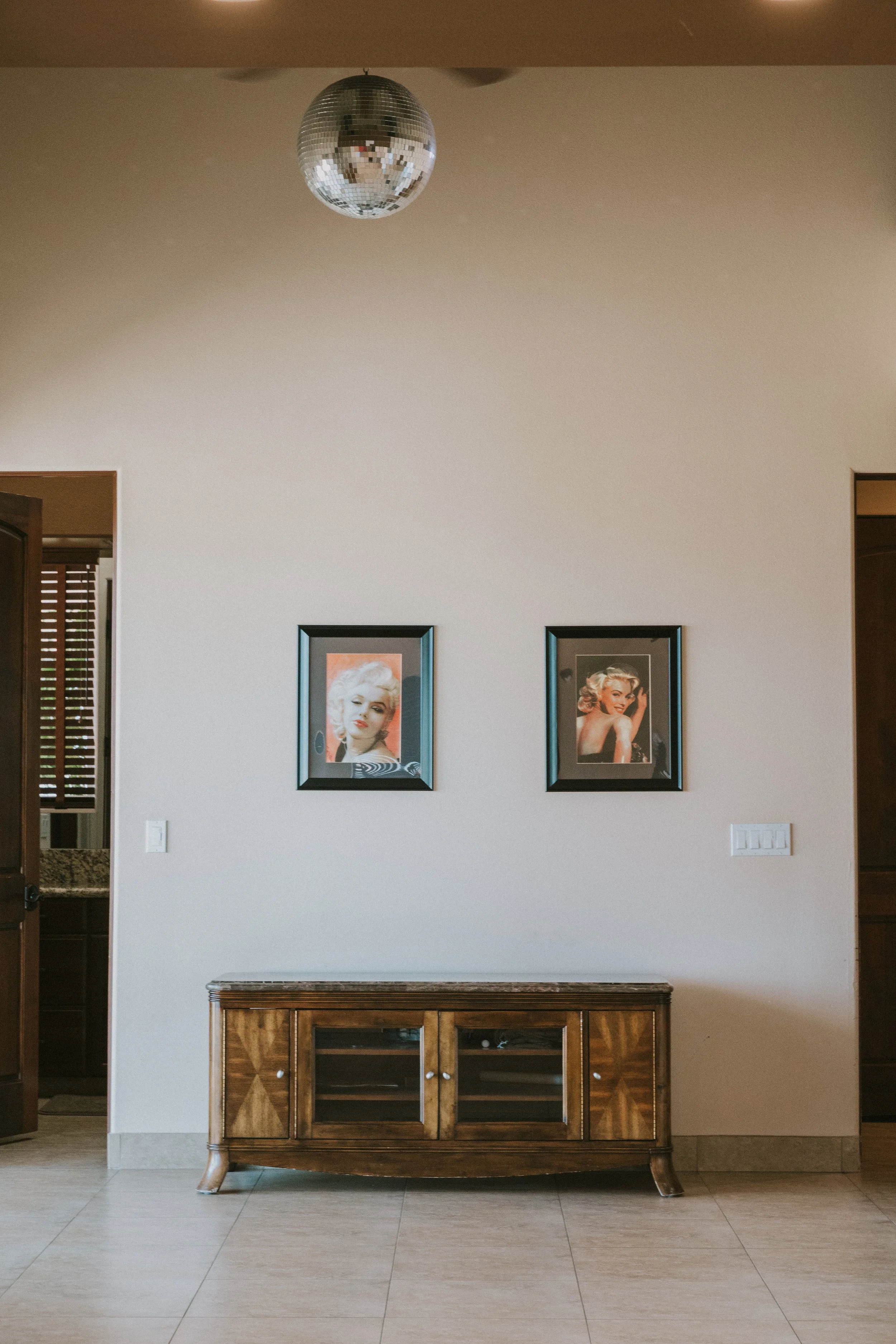 A wooden sideboard against a beige wall with two framed Marilyn Monroe pictures and a ceiling disco ball.