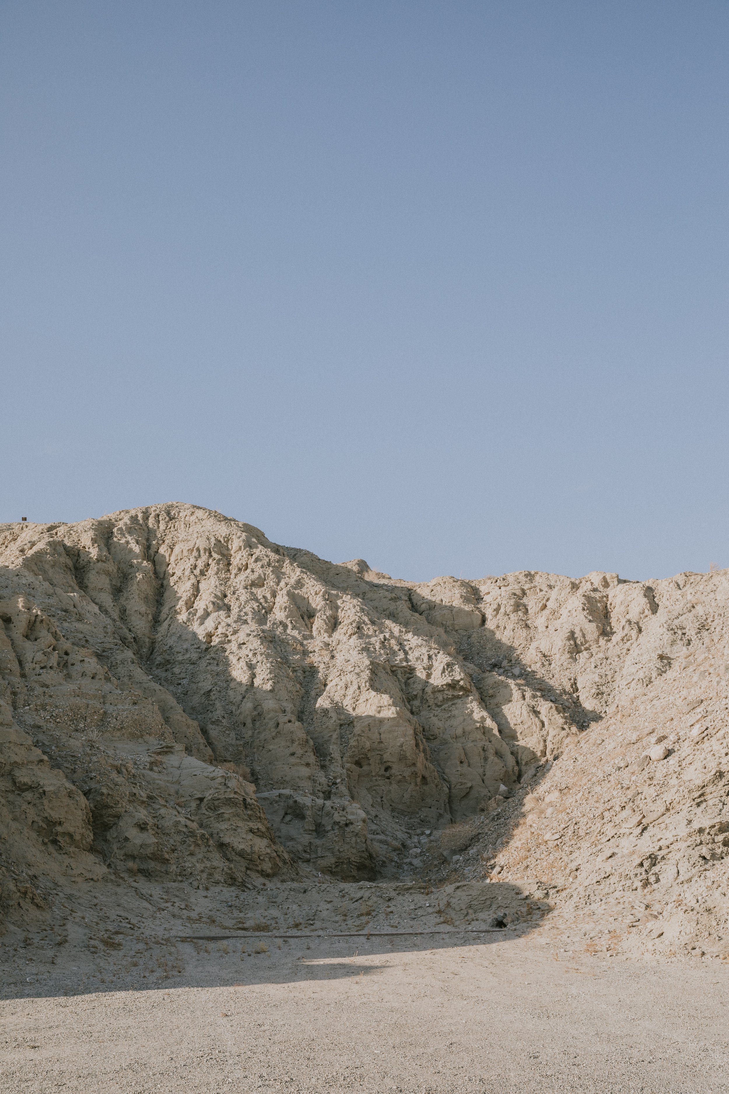 A rugged, arid mountain landscape with light-colored, rocky cliffs under a clear blue sky.