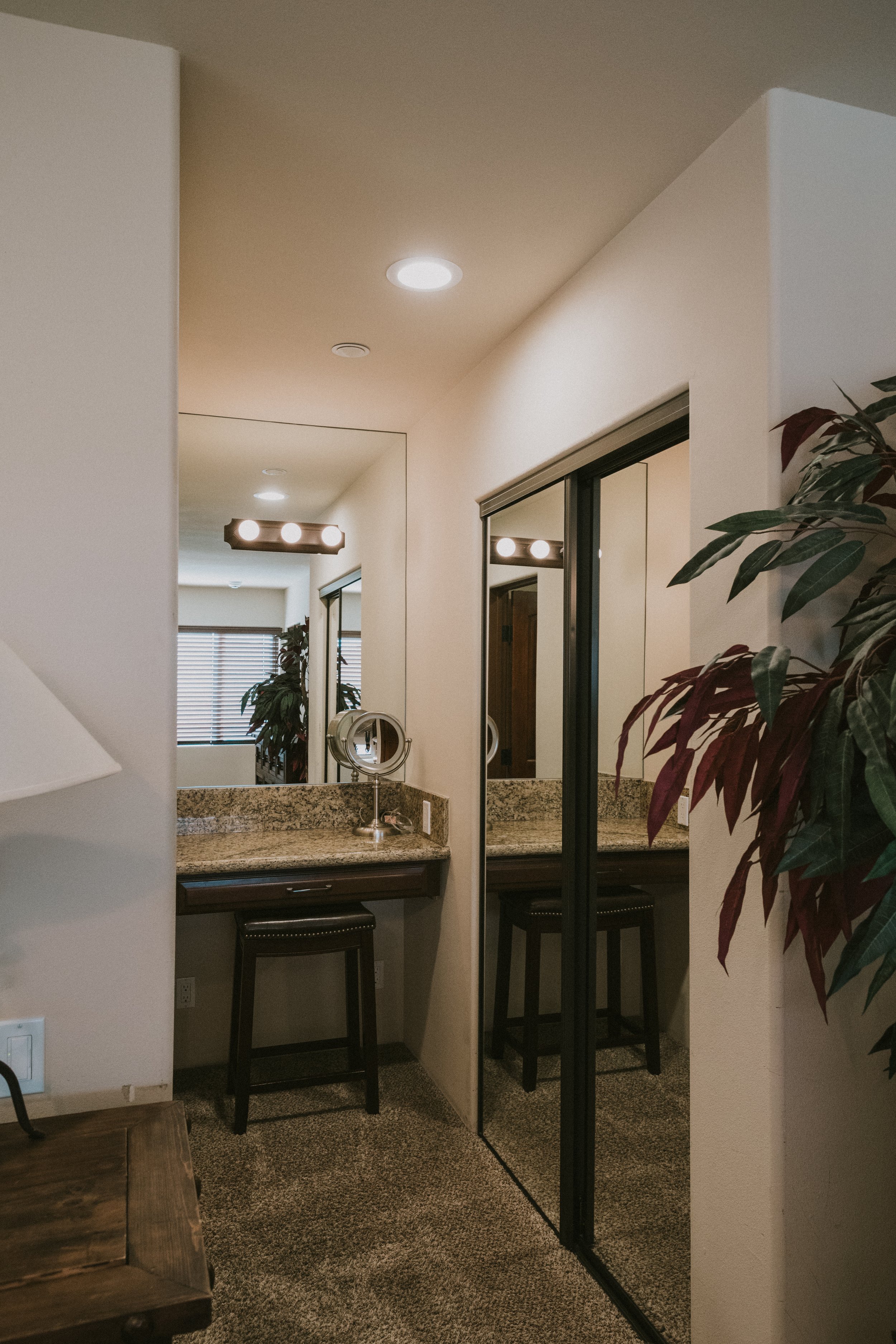 View of a small bathroom area with a granite countertop, mirror, vanity lighting fixture, and a plant in the corner.