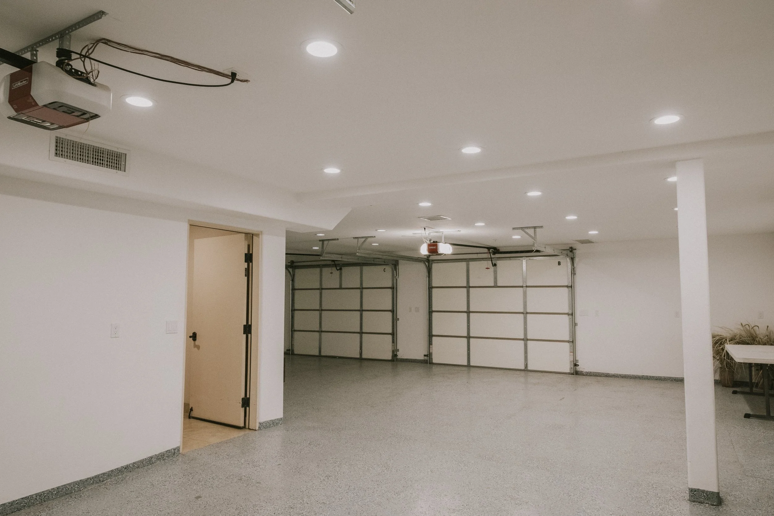 Empty garage with white walls, insulated metal garage door, and ceiling lights.