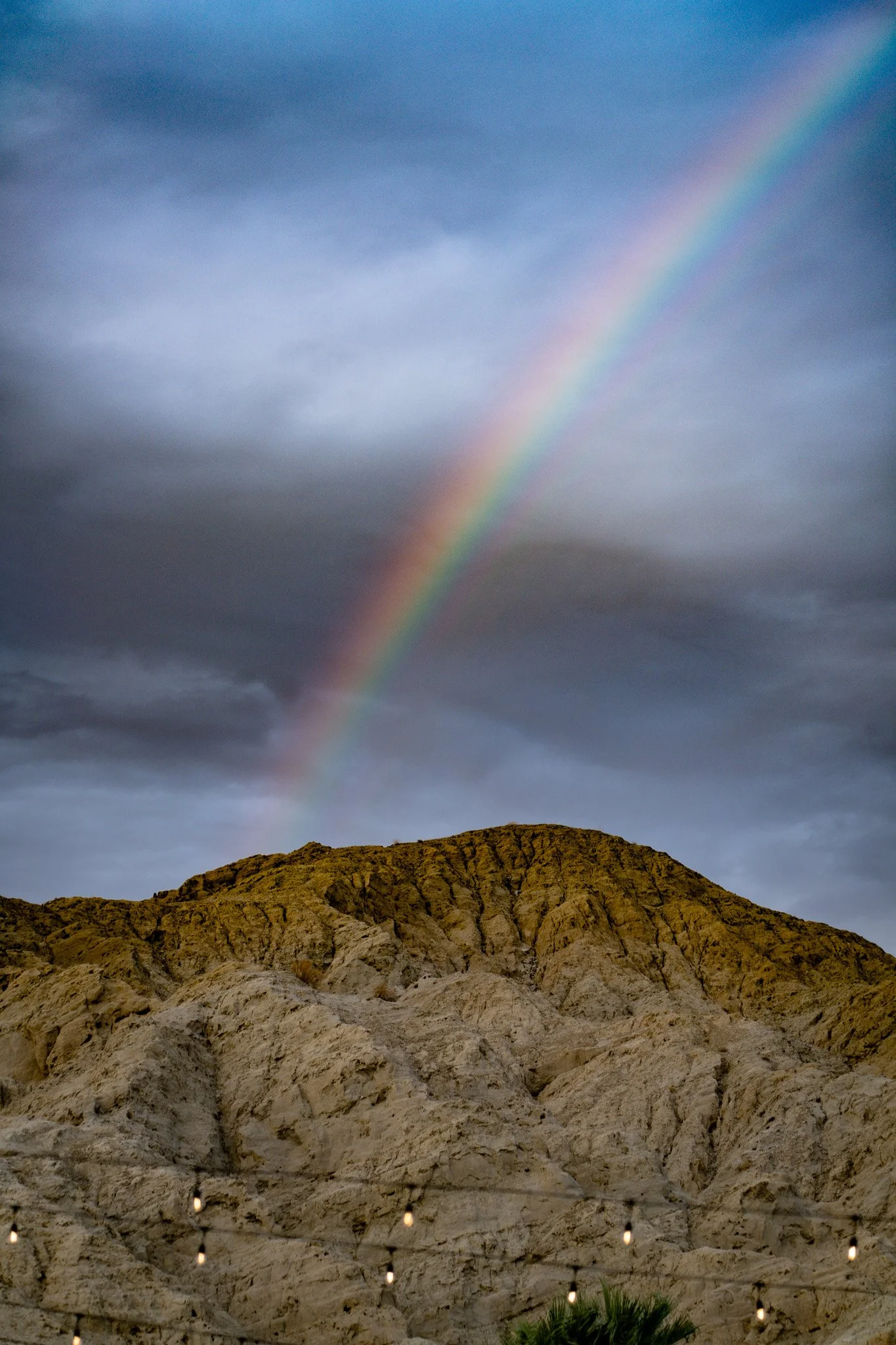 A landscape with a rocky hill or mountain under a cloudy sky, featuring a rainbow arching across the sky.