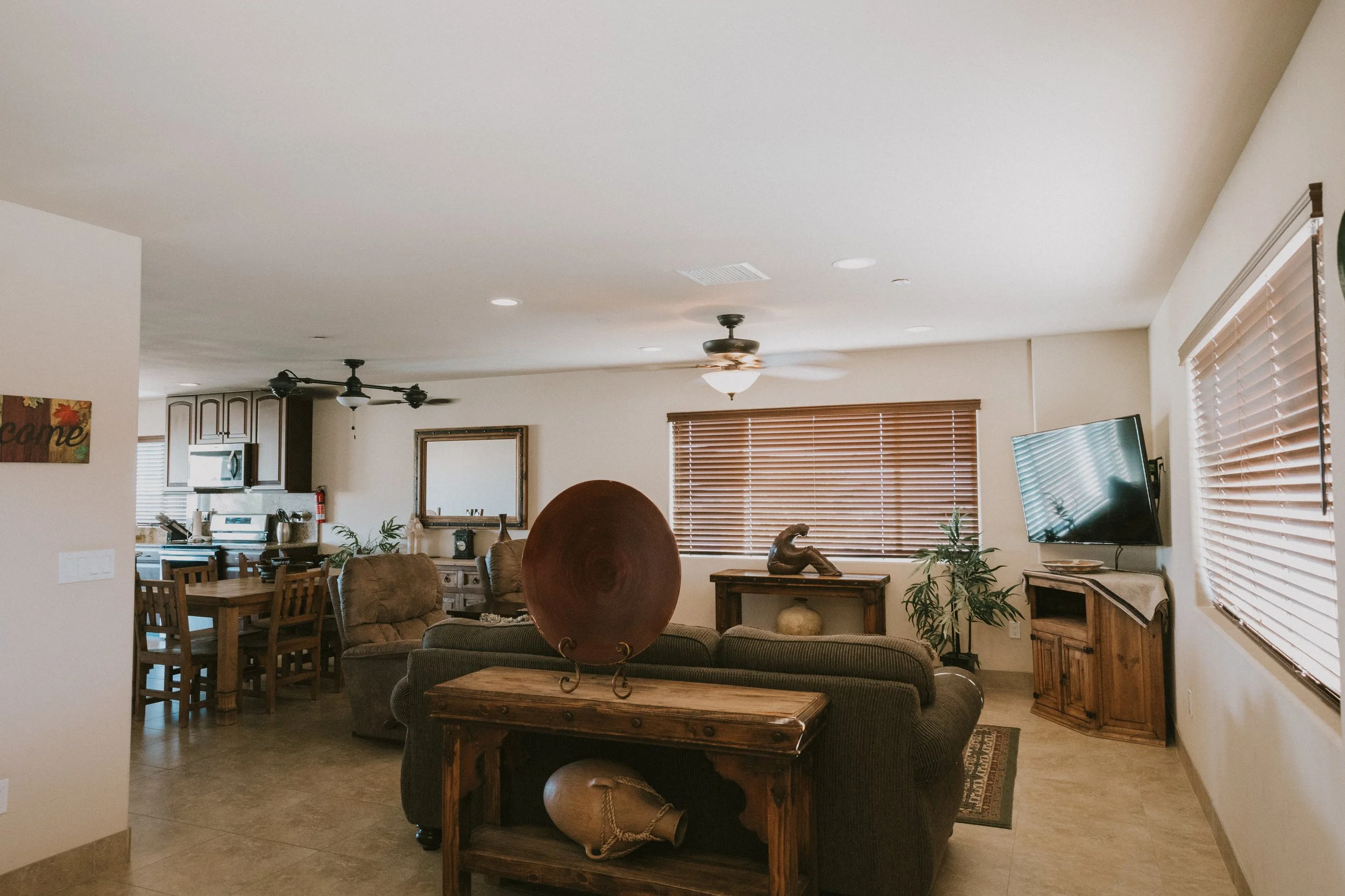 Living room with beige walls, wooden furniture, a flat-screen TV, and windows with wooden blinds.