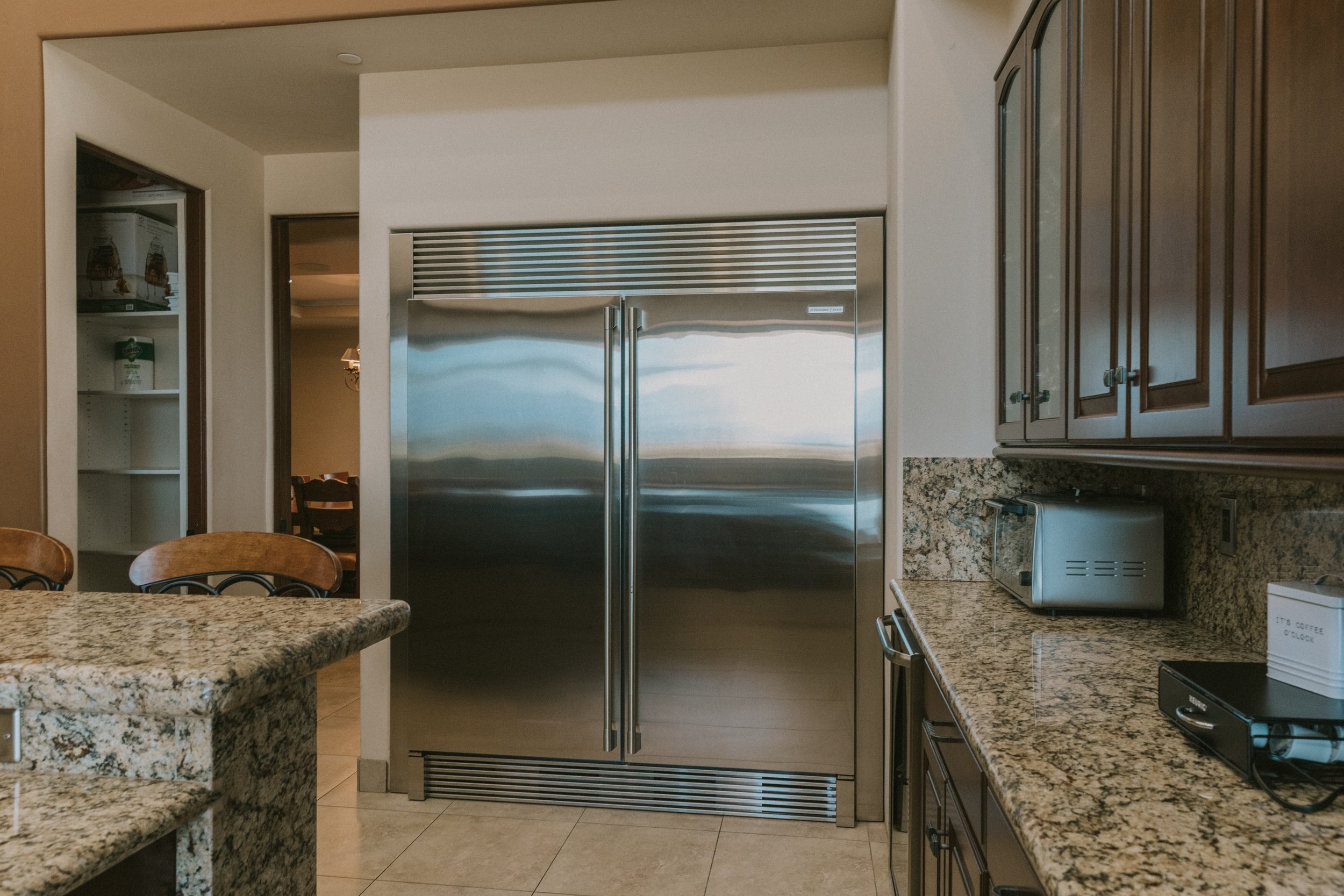 Kitchen with granite countertops, a stainless steel refrigerator, wooden cabinetry, a microwave, and a granite island.