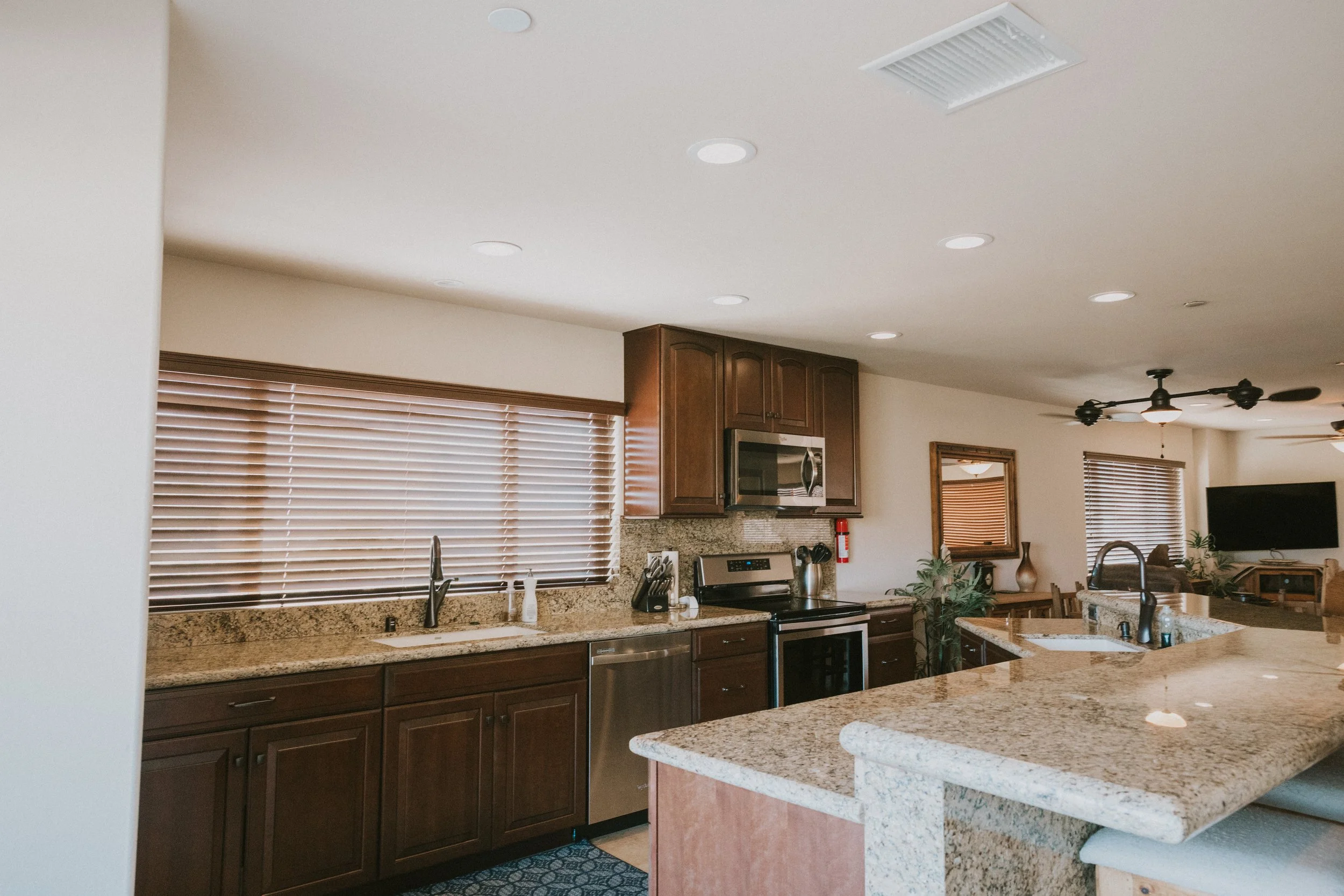 Kitchen with wooden cabinets, granite countertops, and a window with horizontal blinds. Stainless steel appliances and a ceiling fan are also visible.