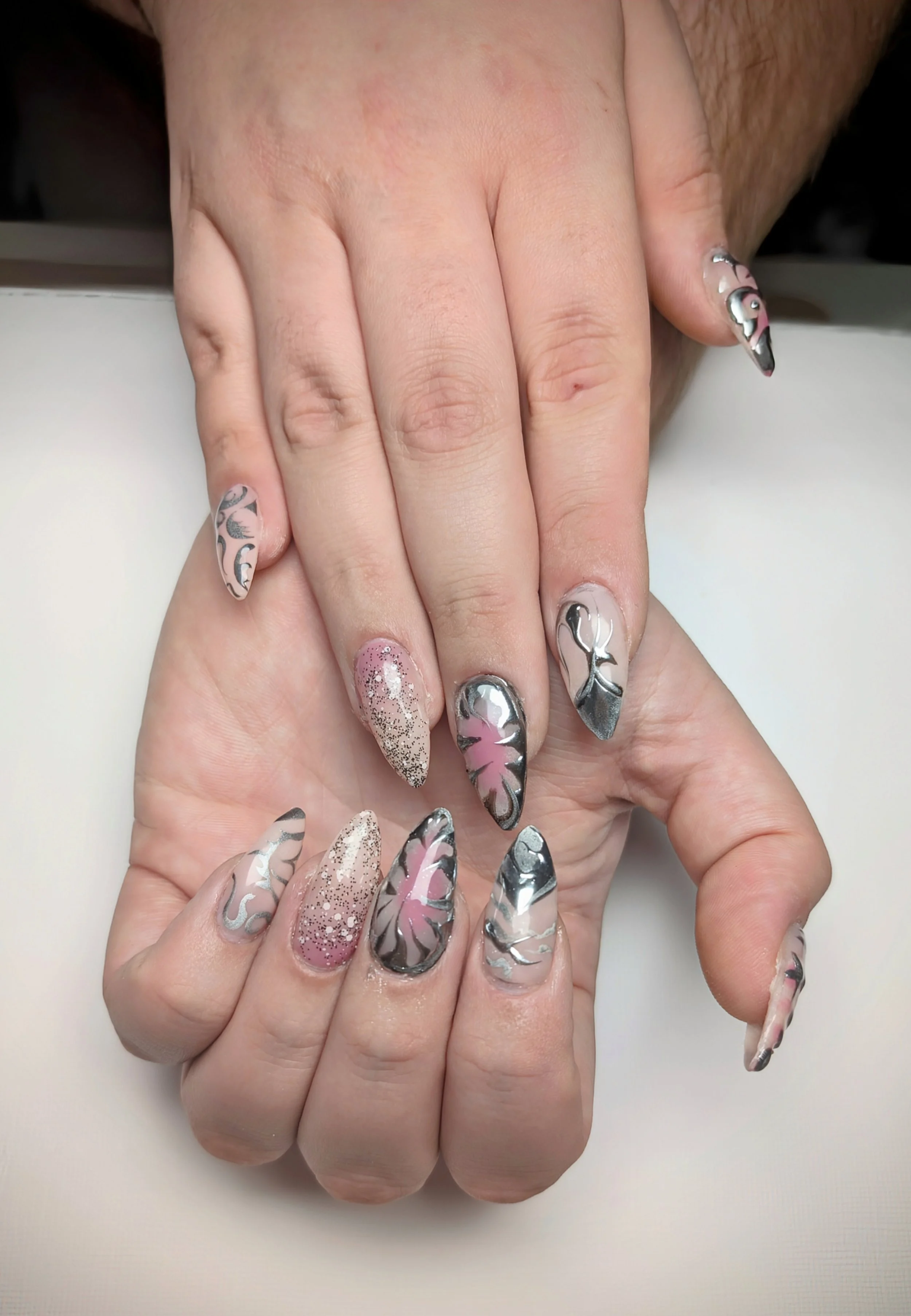 Close-up of two hands with manicured nails featuring intricate designs in pink, black, silver, and glitter patterns.