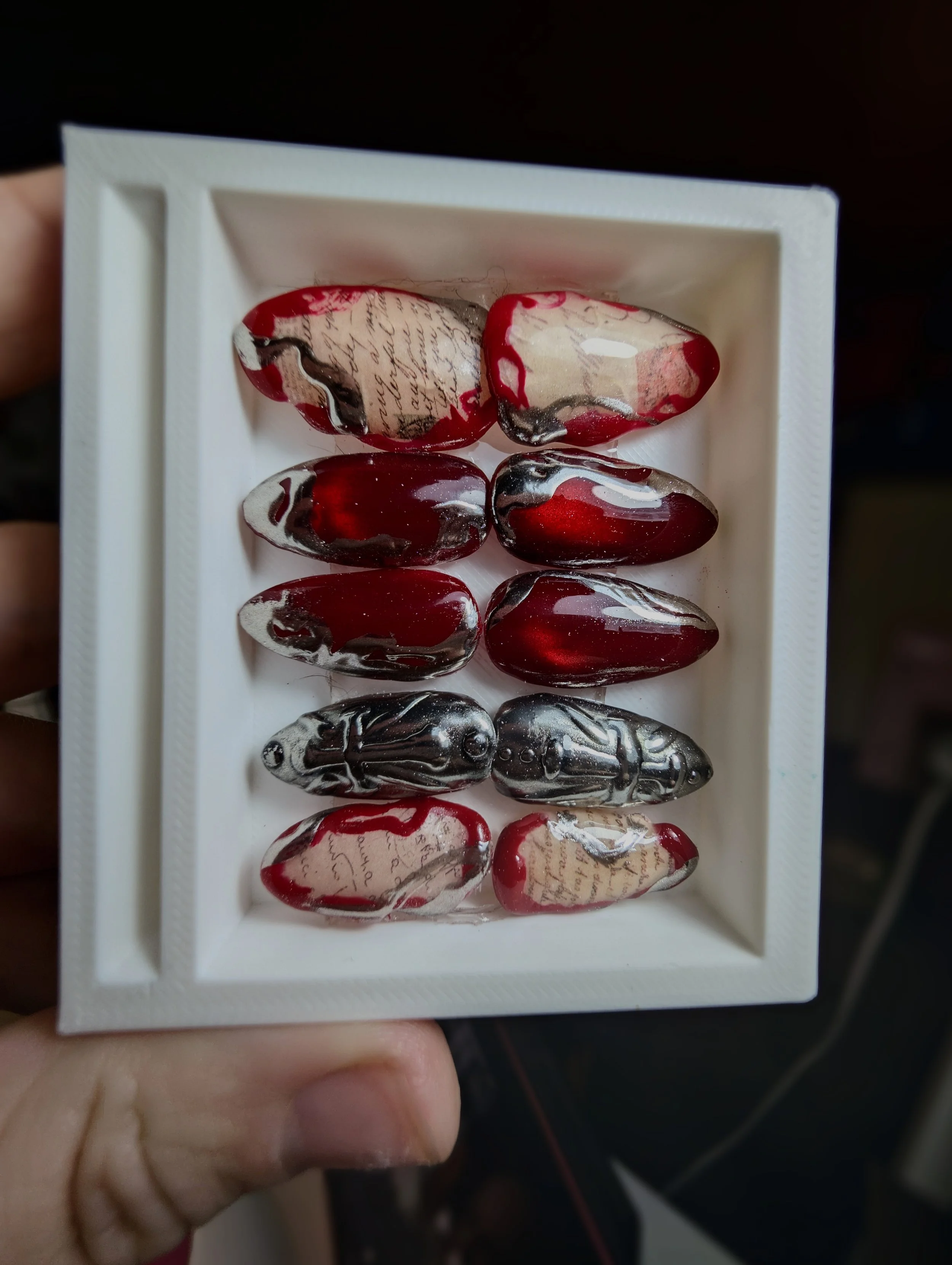 A white box containing several marbled gemstone pieces with a blend of red, black, cream, and white colors and script writing patterns on some.