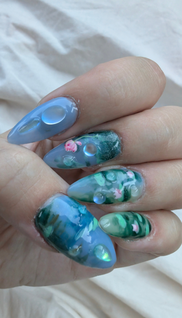 Close-up of a hand with long, decorated acrylic nails featuring a nature-inspired design with blue, green, pink, and white colors, and bubble and flower motifs.