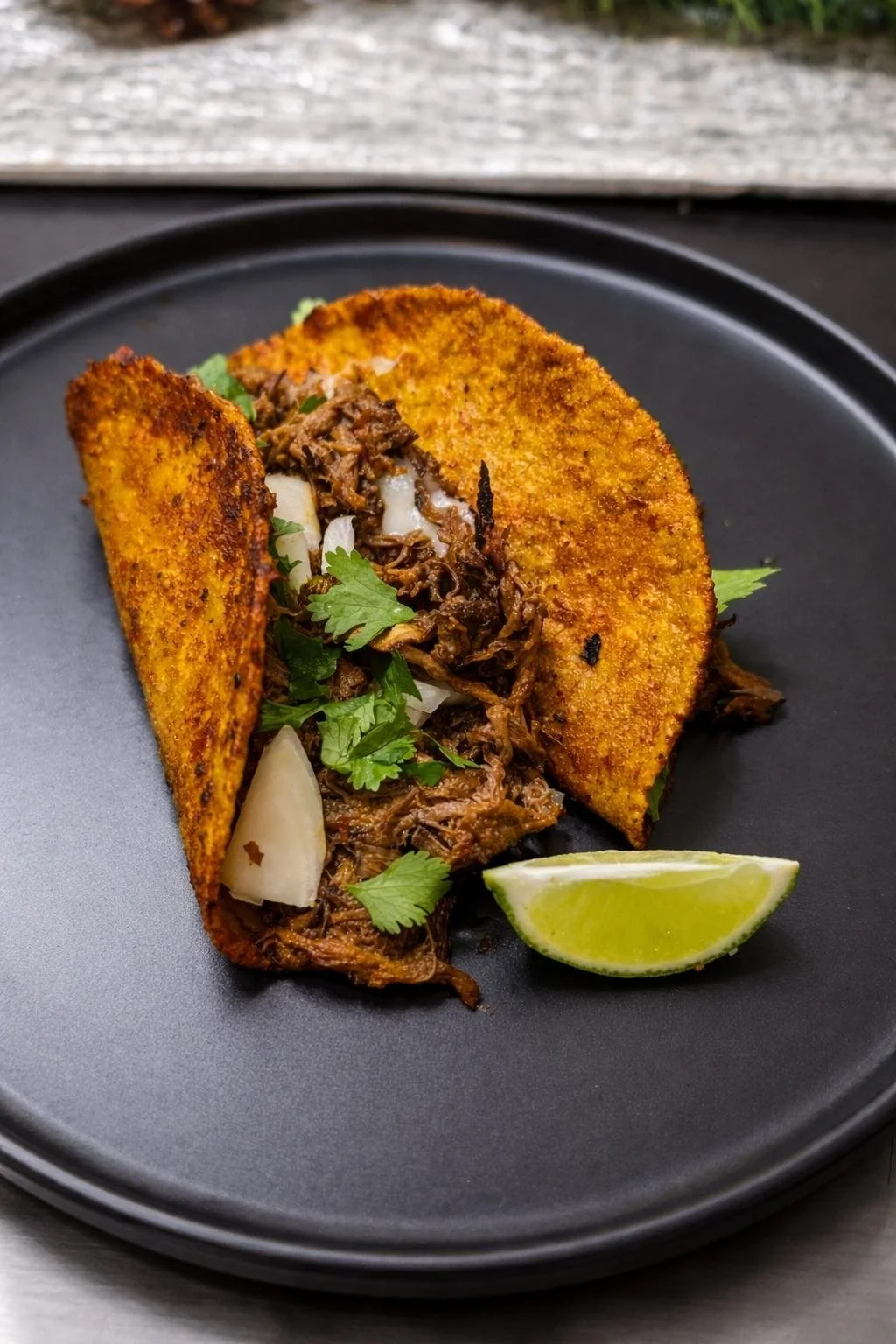 A taco with shredded meat, cilantro, onion, and a lime wedge on a black plate.