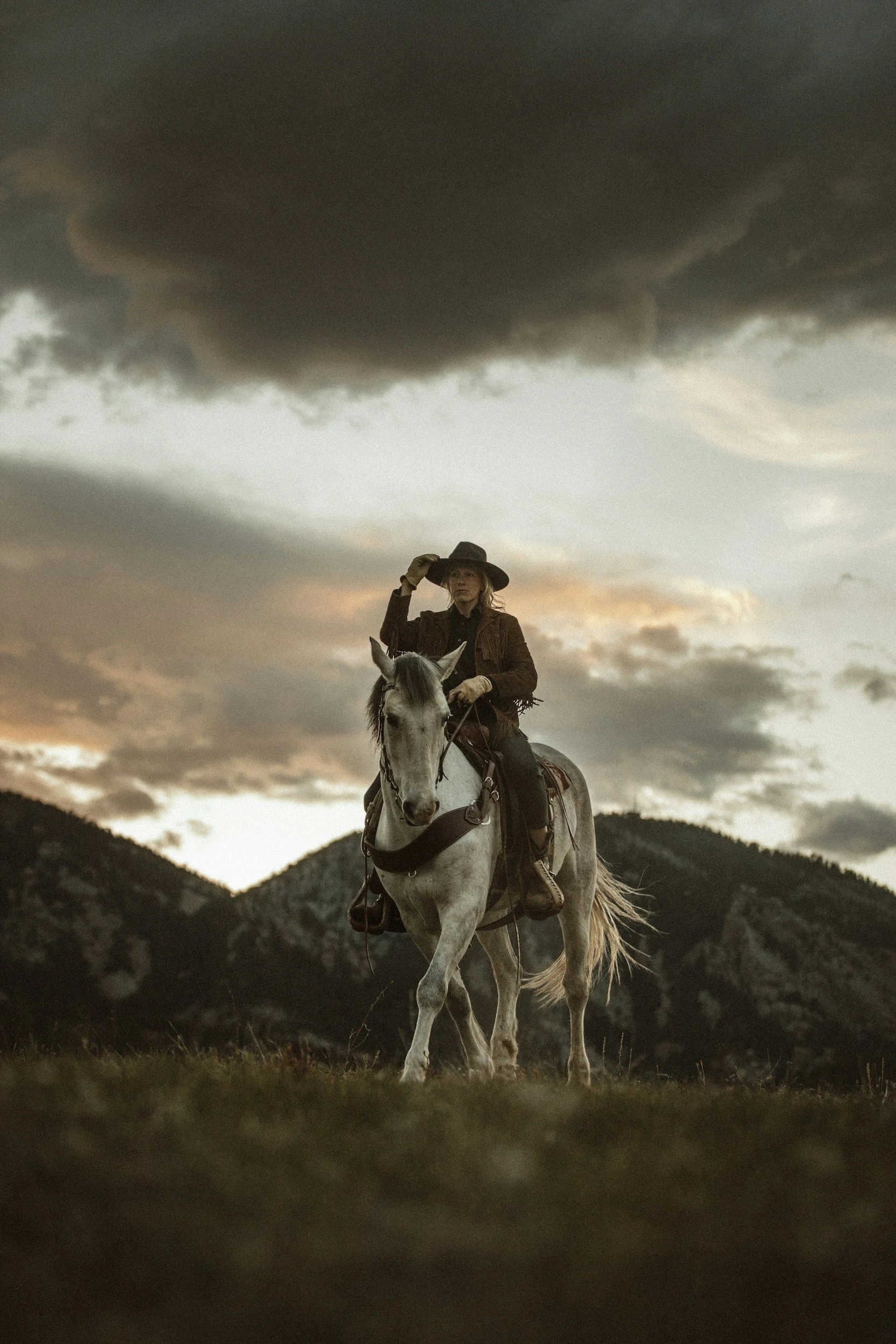 A cowgirl rides her grey horse through the mountains of Montana