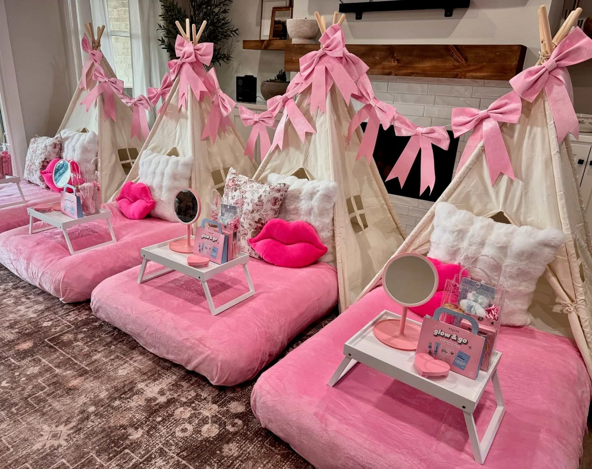 Three pink and white indoor tents with pillows, trays, mirrors, and spa kits set up for a girls’ sleepover party in a living room.