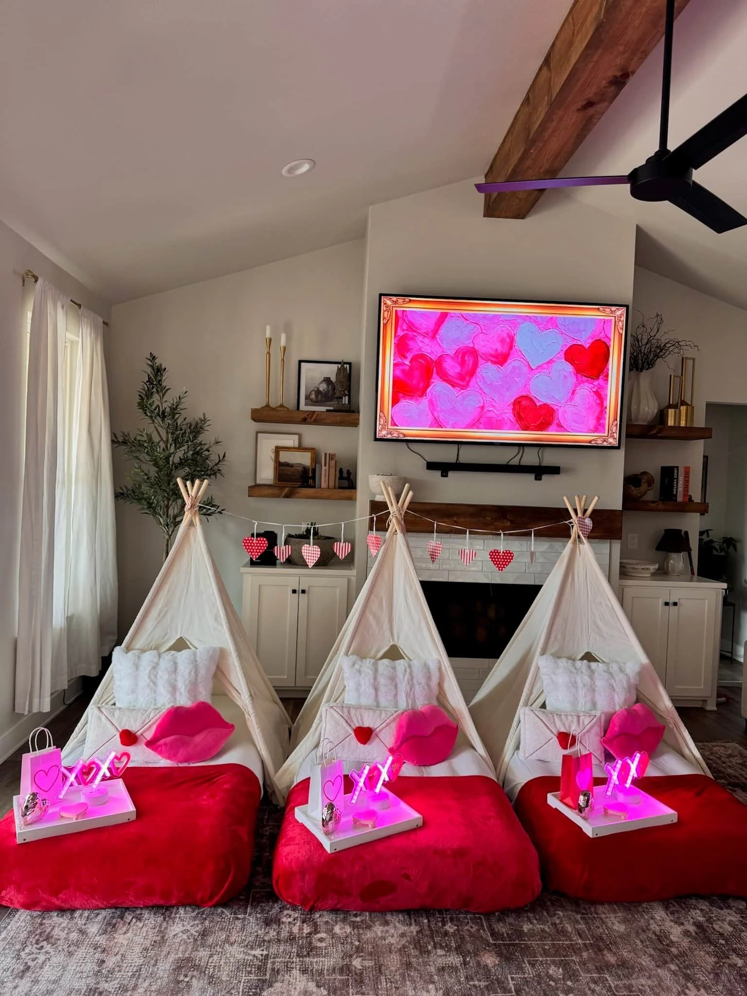 Three small indoor tents with red blankets, pink heart pillows, and Valentine decorations, set up for a cozy celebration in a living room.