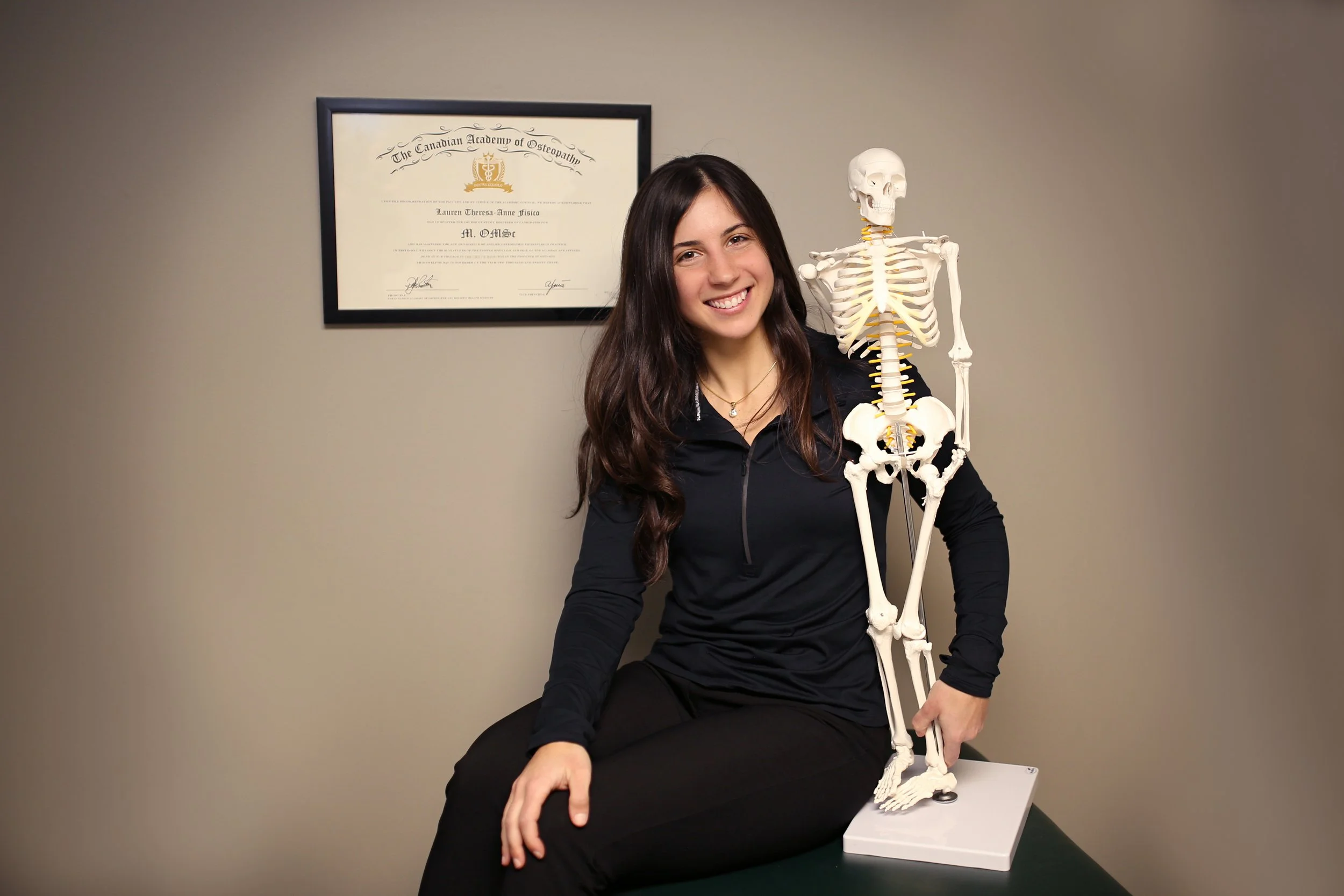 osteopathy business owner smiling with her masters degree with a skeleton in Lasalle and windsor Essex ontario