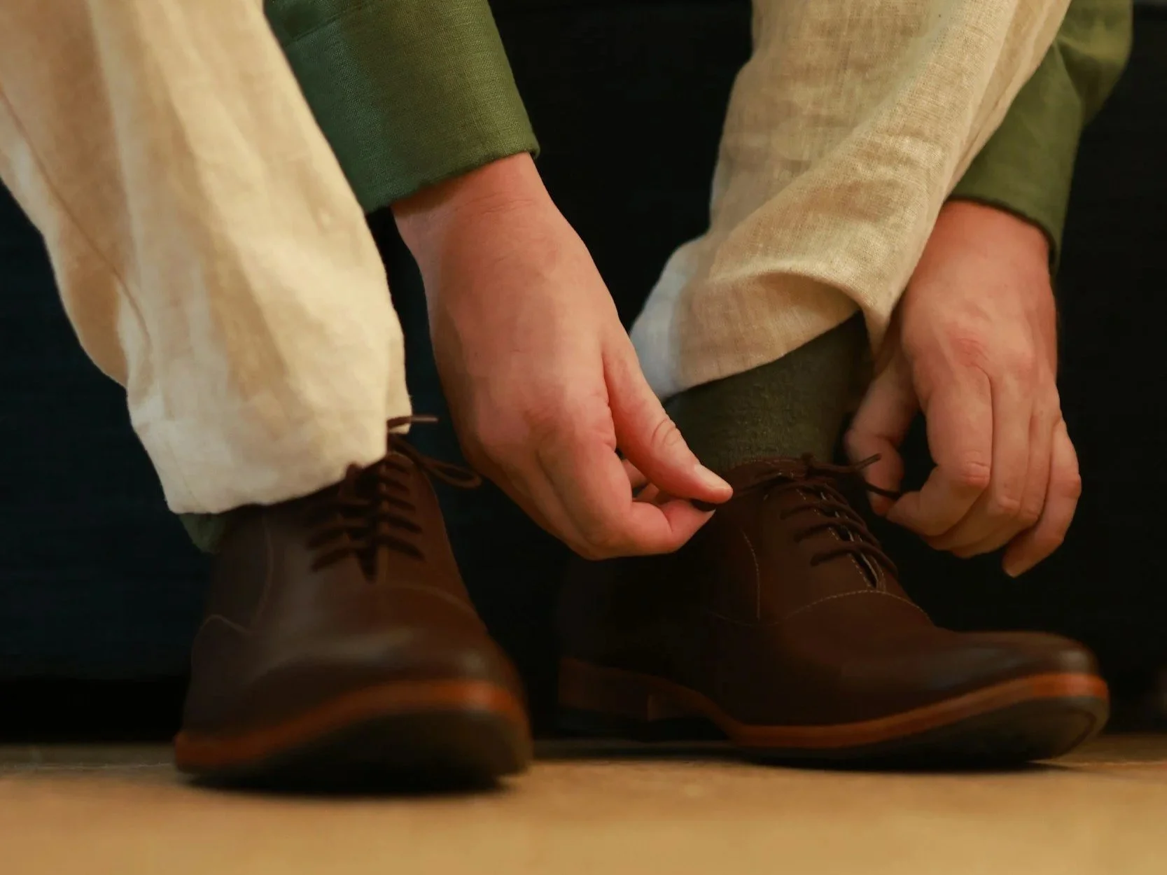 Person tying shoelaces on brown leather dress shoes.