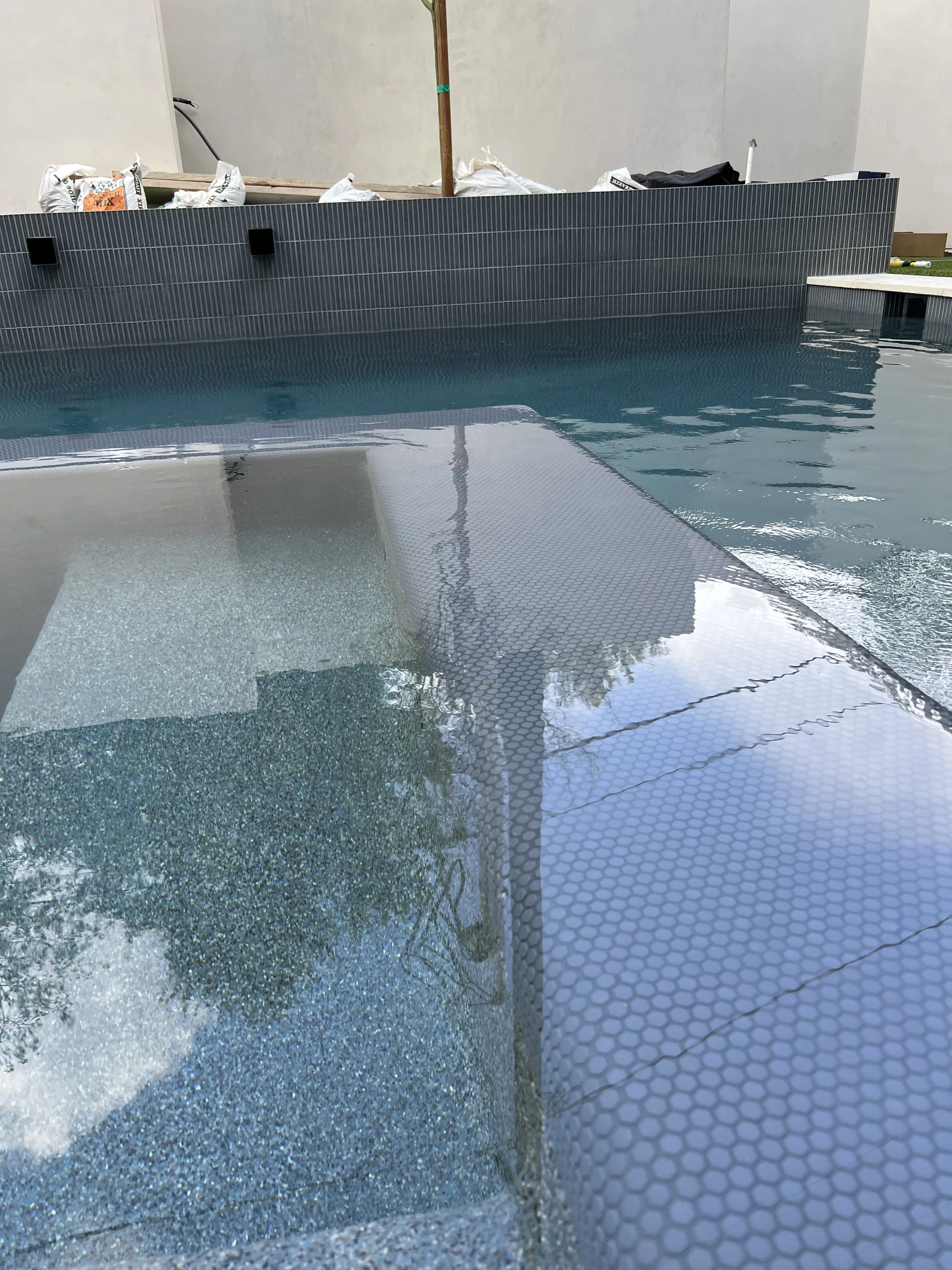 Close-up of a modern swimming pool with textured tile edge, reflecting the sky and surroundings.