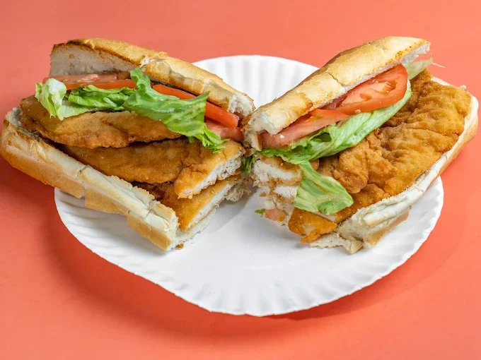 Fried fish sandwich with lettuce, tomato, and bread on a white paper plate