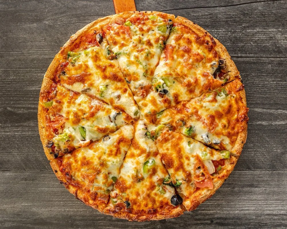A whole cheese and vegetable pizza on a wooden surface.