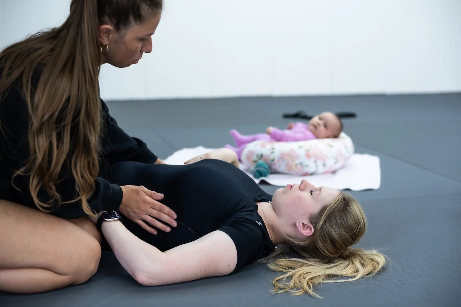 Asia coaching a new mom through core and breathing work while her baby rests nearby
