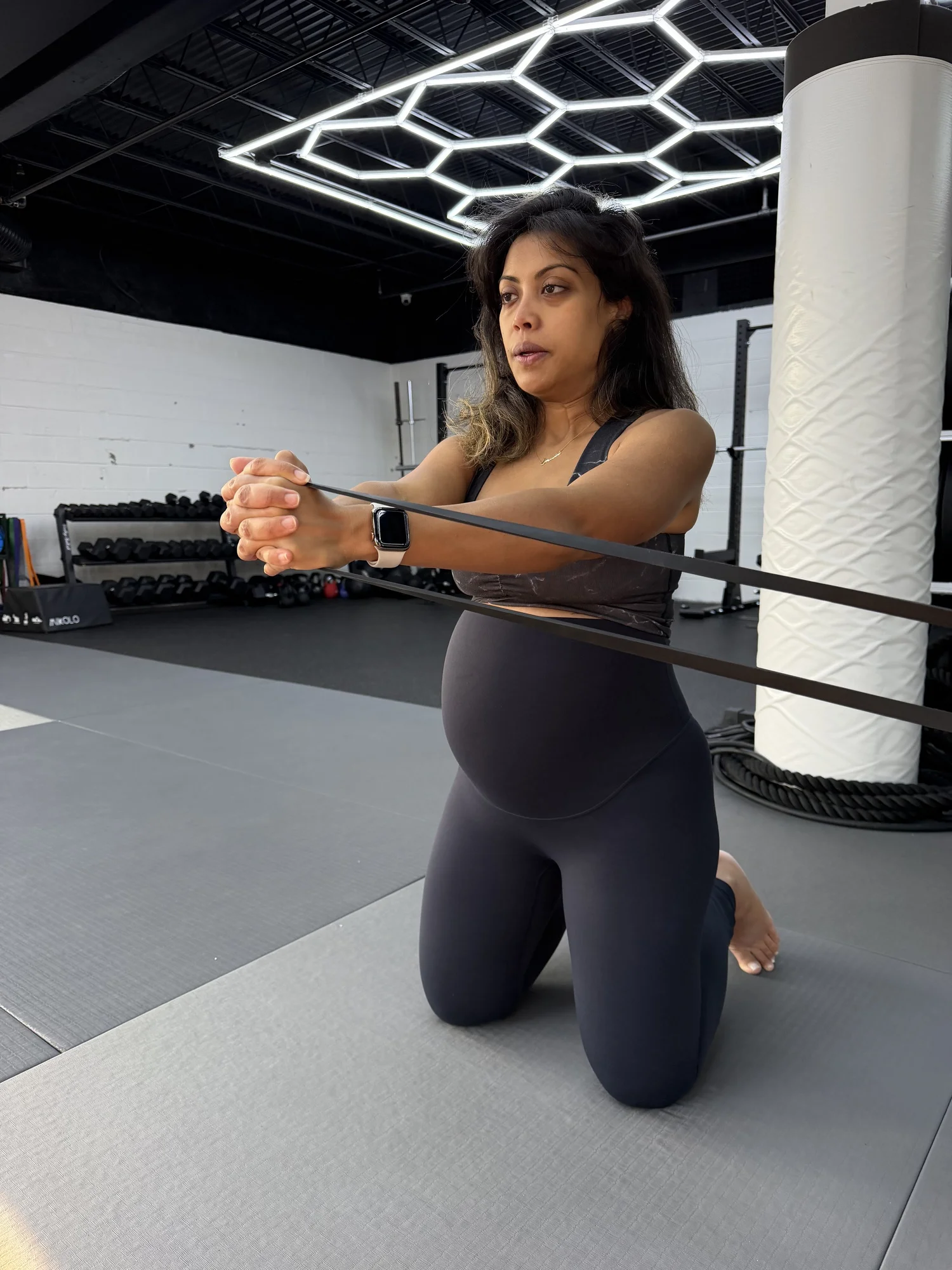 Pregnant woman doing a kneeling resistance-band row during a prenatal strength session