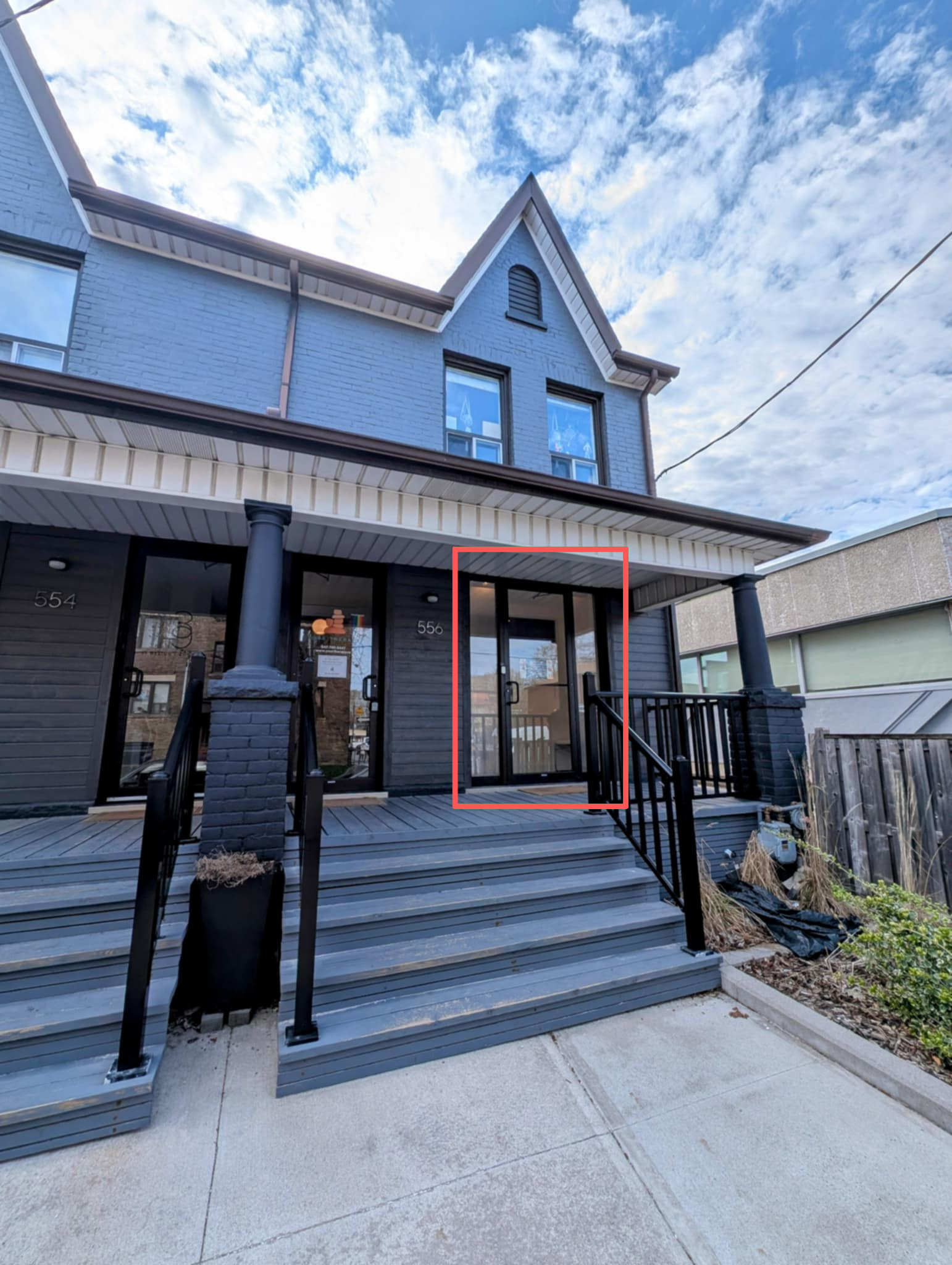 Building with a staircase leading to glass door entrance, black railing, dark exterior siding, and a blue sky with clouds.