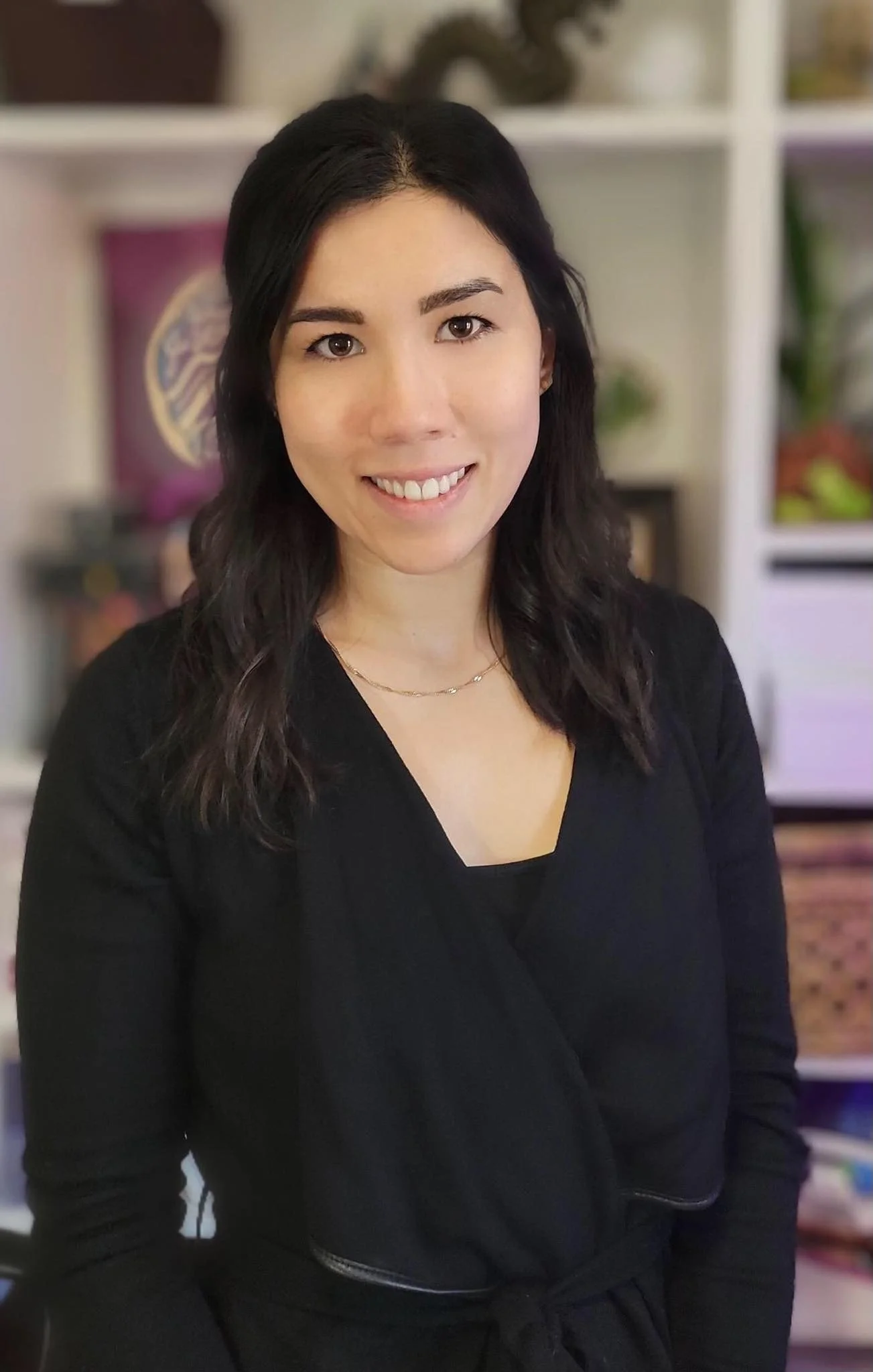 Melodie Lemay-Gaulin. A woman with shoulder-length dark hair wearing a black outfit, smiling indoors with shelves containing books, plants, and decorative items in the background.