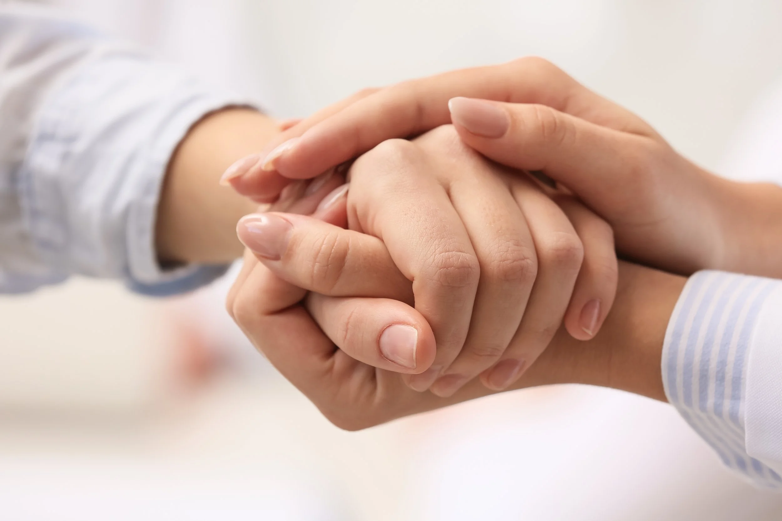Two people holding hands, one with a slightly darker skin tone and the other with a lighter skin tone, both wearing long-sleeved shirts.
