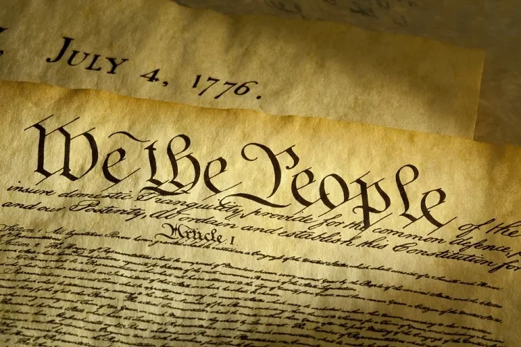 Close-up of an aged historical document, with the phrase 'We the People' written at the top and a date of July 4, 1776, visible on the page.