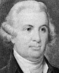 Black and white portrait of a man with wavy white hair wearing a dark coat and white shirt
