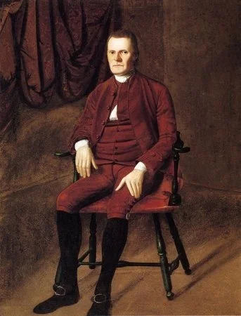A portrait of a man sitting on a wooden chair in front of a dark background with draped curtains. He is dressed in a red coat with gold buttons, a white shirt, and black stockings.