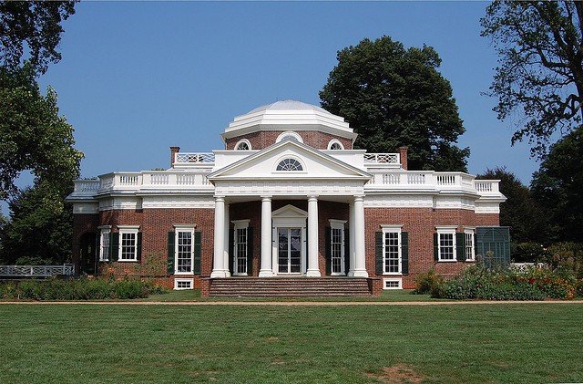 Large historic mansion with brick exterior, white columns, and a domed roof, surrounded by trees and a well-maintained lawn.