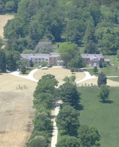 An aerial view of a large estate with a main house, surrounding greenery, trees, and fields.