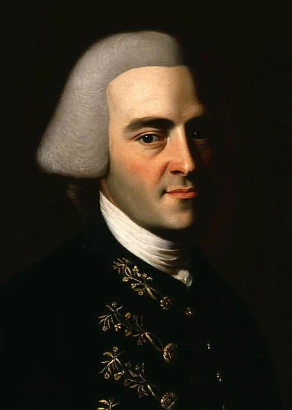 Portrait of a man with gray 18th-century style wig, wearing a dark coat with gold embroidery and a white cravat.