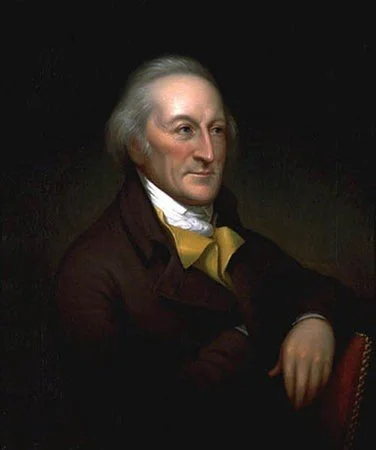 Portrait of a man with white hair, wearing a dark coat and a cravat, seated with one arm resting on a chair, against a dark background.
