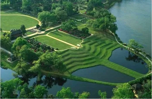 Aerial view of a landscaped park with walking paths, green lawns, trees, and water features, including two small lakes.