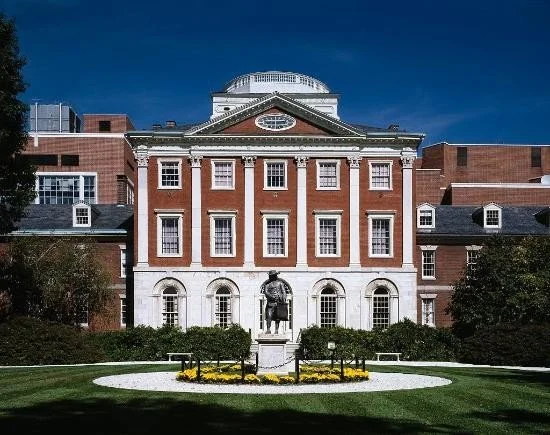 Front view of a historic brick building with white accents, a central statue of a man on horseback, and well-maintained lawn and landscaping under a blue sky.