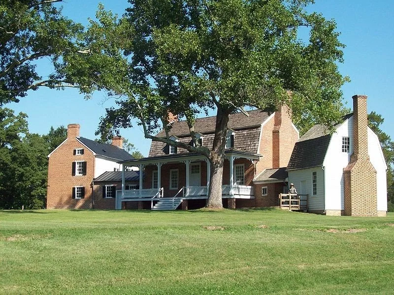 Brick and white house with a large tree in front, surrounded by green lawn under a clear blue sky.