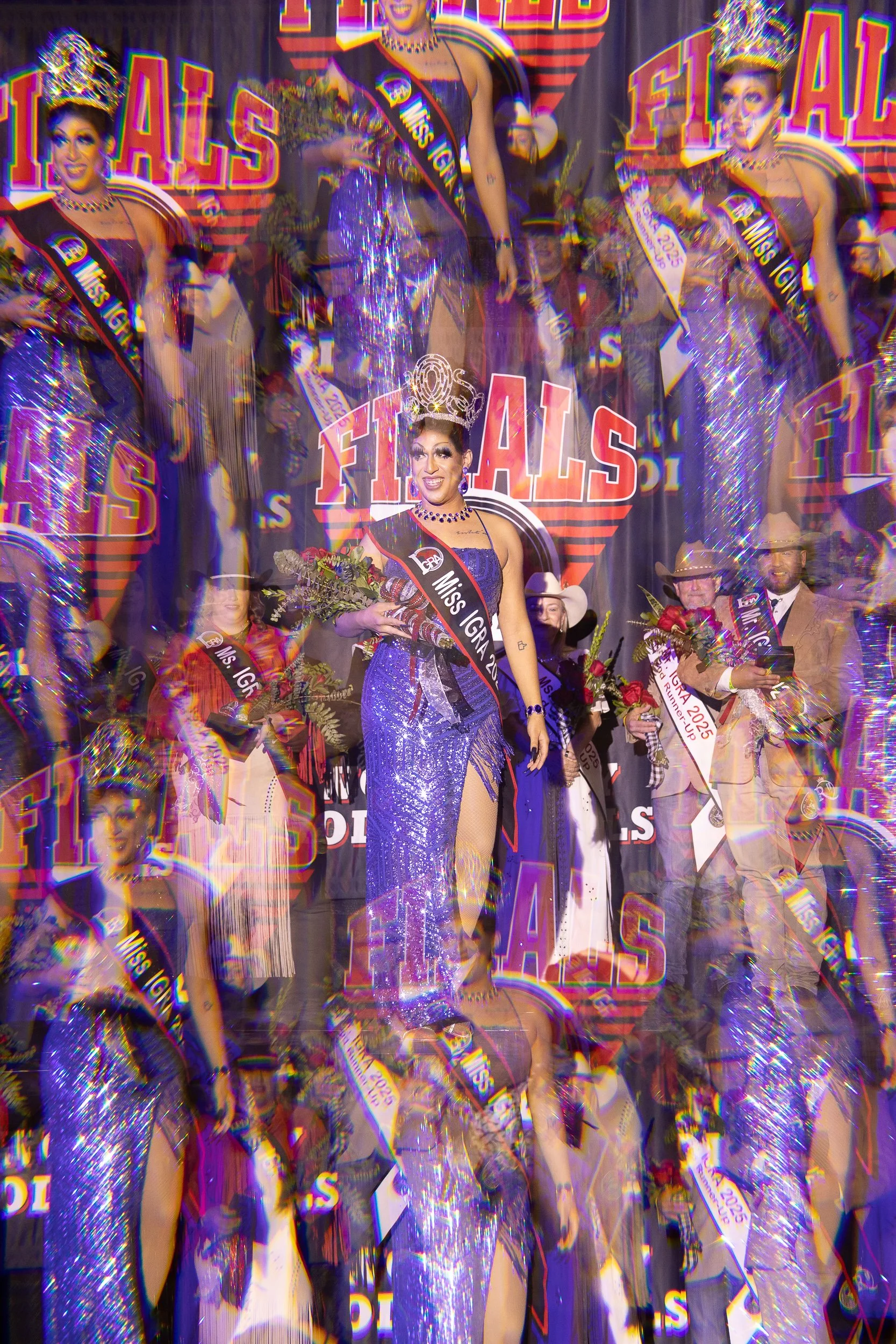 A beauty pageant winner on stage during a celebration, wearing a sparkling purple gown, a crown, holding a bouquet of flowers, and wearing a sash that reads "Miss IGRA 2023." The backdrop reads "Finals," and several other contestants and individuals 