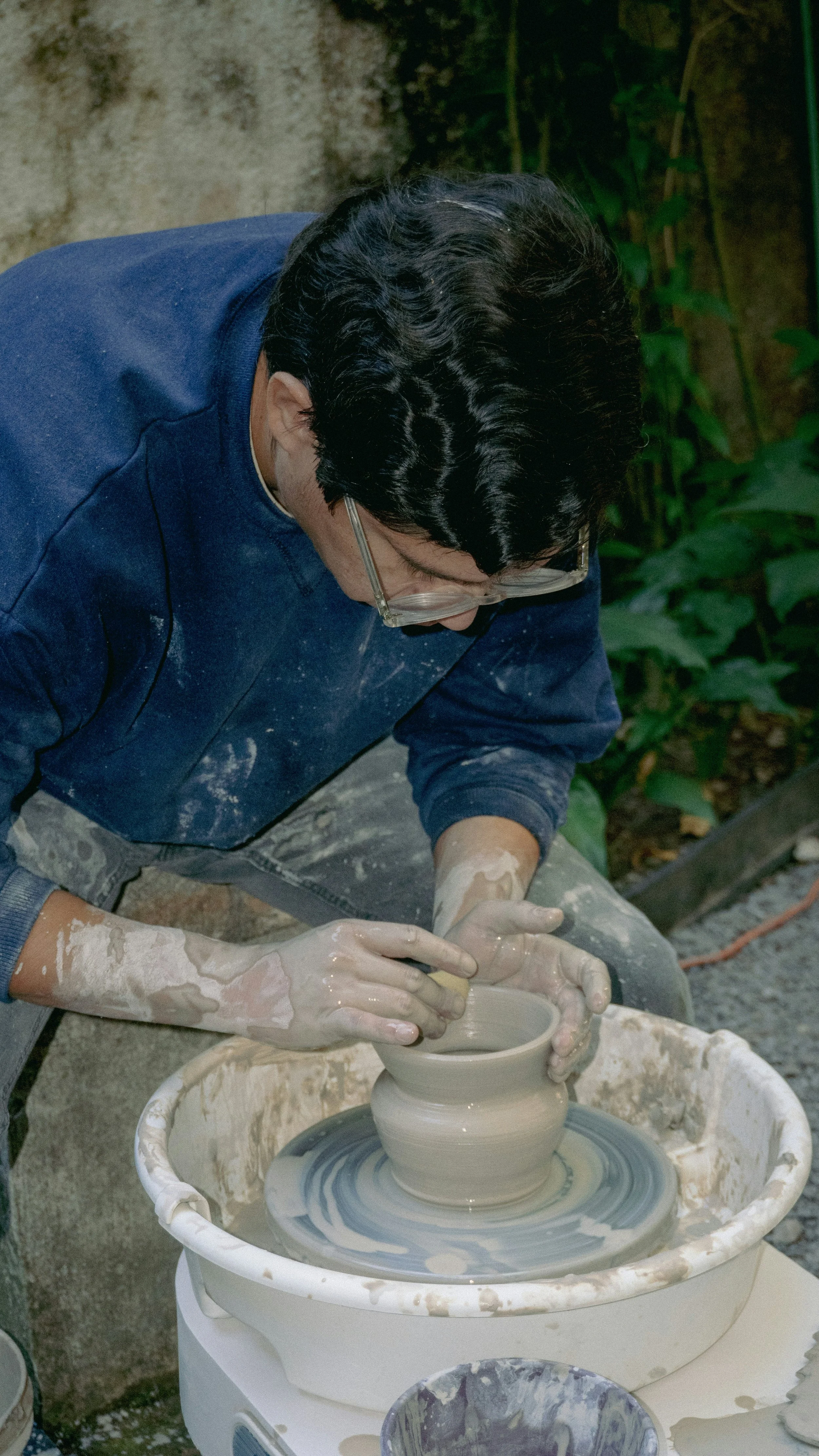 Man shaping a clay pot on a pottery wheel outdoors.